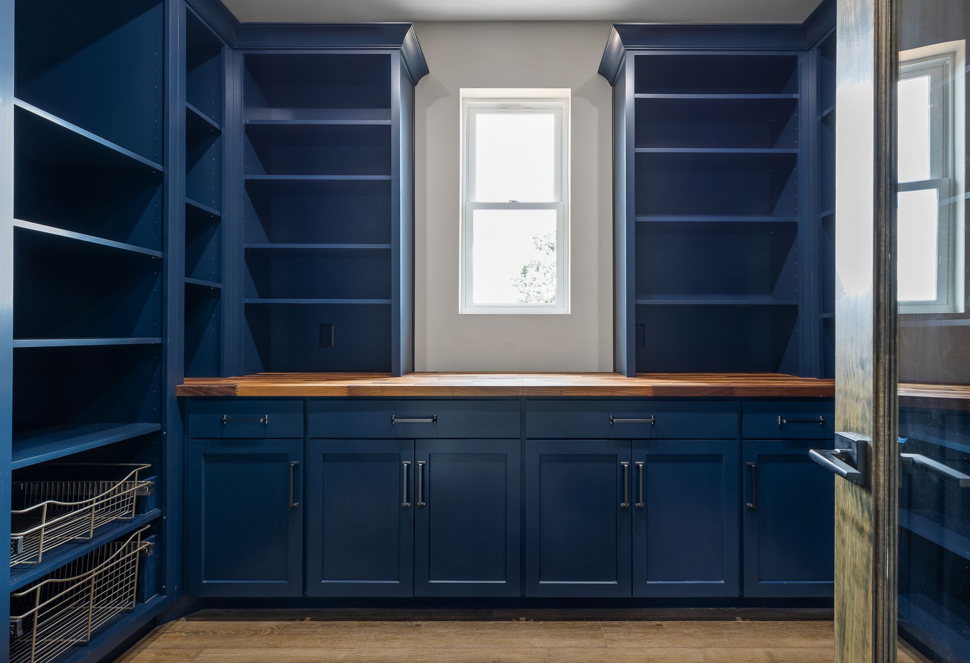 Blue pantry with wooden countertop, cabinets, and shelves; window in the center.