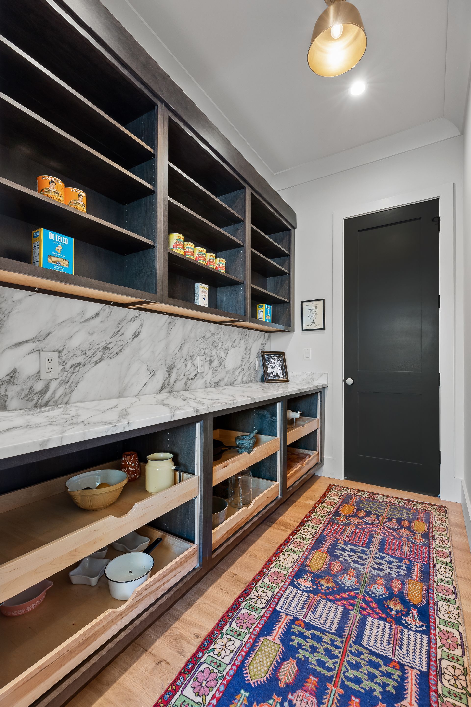 Pantry with dark shelves, marble countertop, and a colorful rug; a black door is visible.