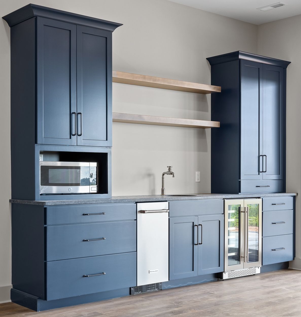 Blue built-in bar with cabinets, microwave, dishwasher, and refrigerator. Two wooden shelves are mounted above the counter.