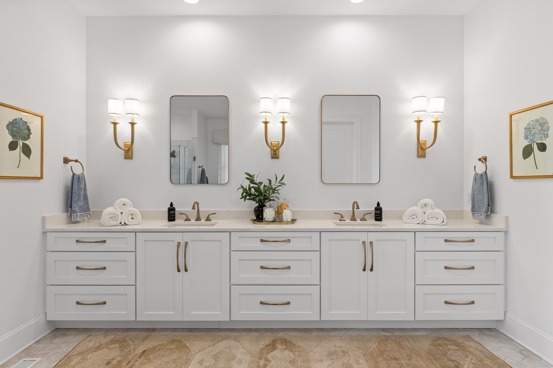 White bathroom with double vanity, mirrors, sconces, and framed artwork.