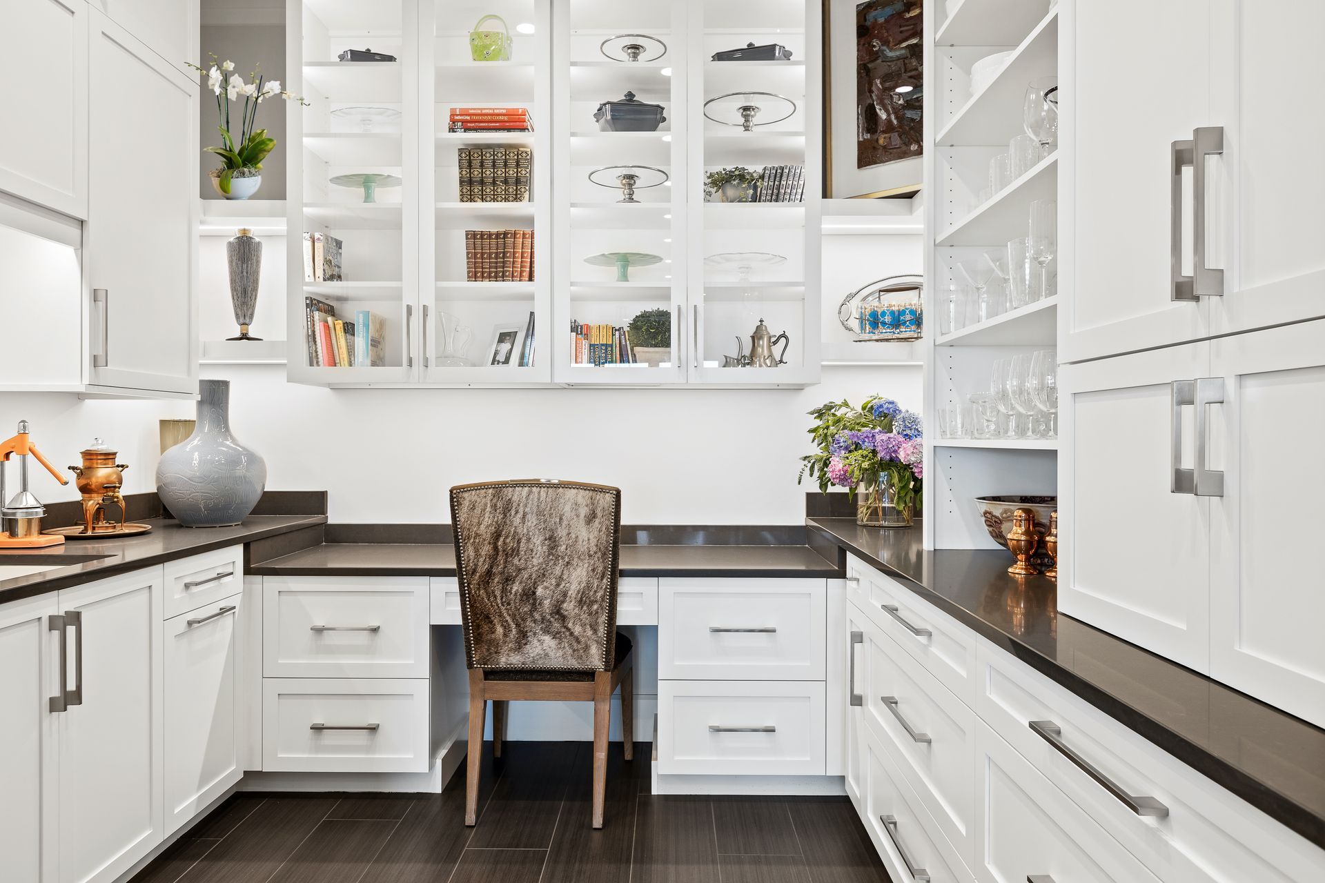White kitchen with built-in desk, cabinets, dark countertops, and a patterned chair.