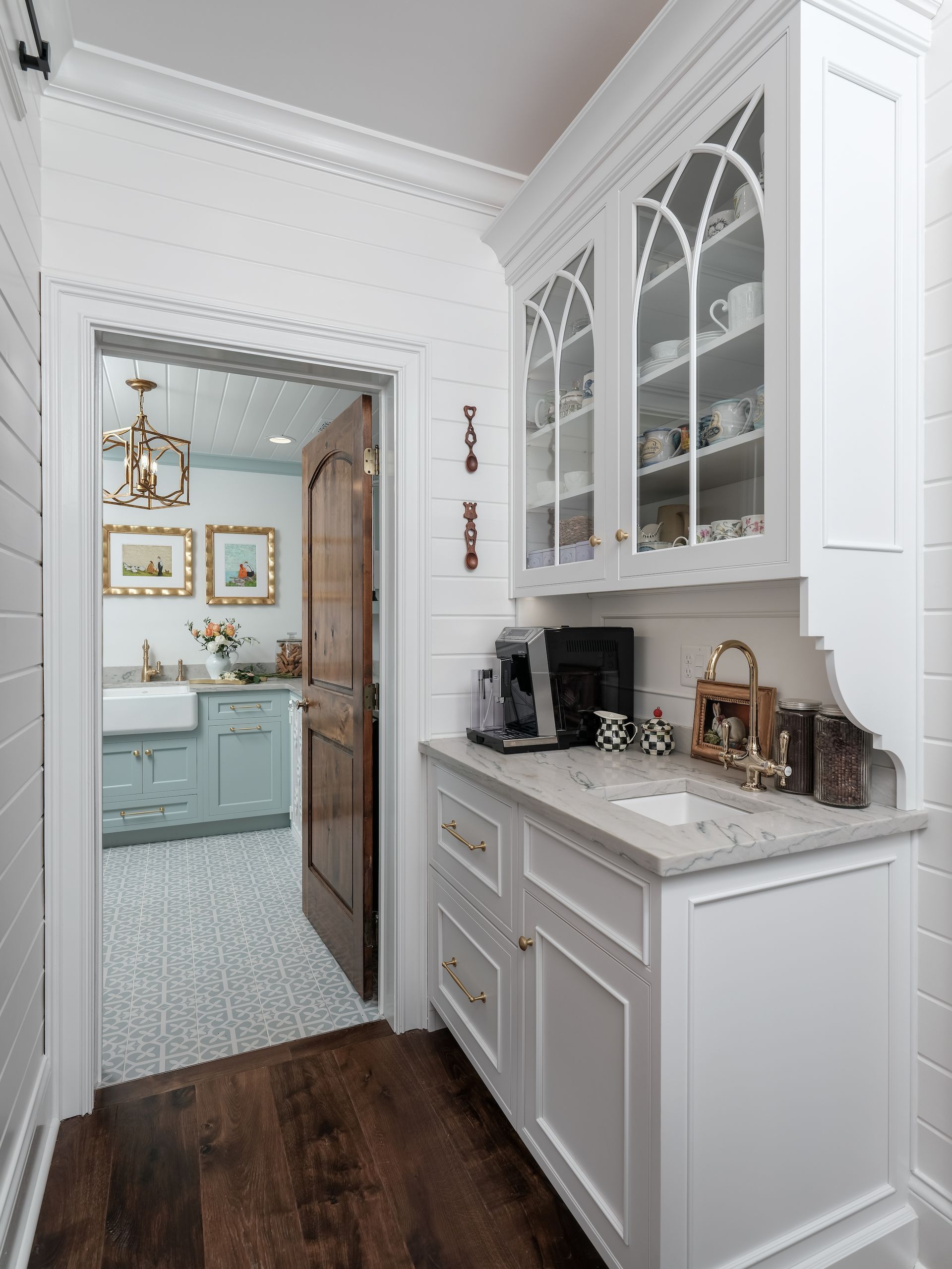 White kitchen area with a coffee station, a door to a powder room, and wooden floors.