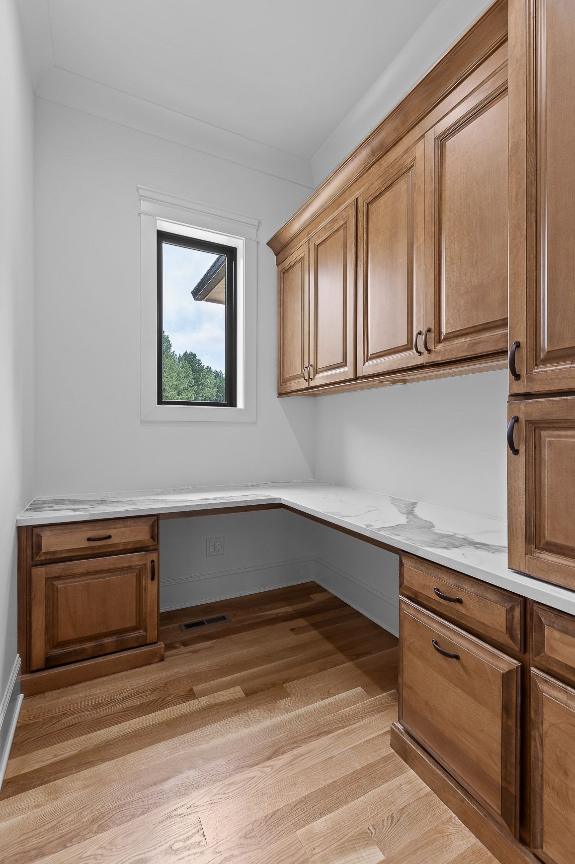 Office space with wooden cabinets, a white countertop desk, and a window.