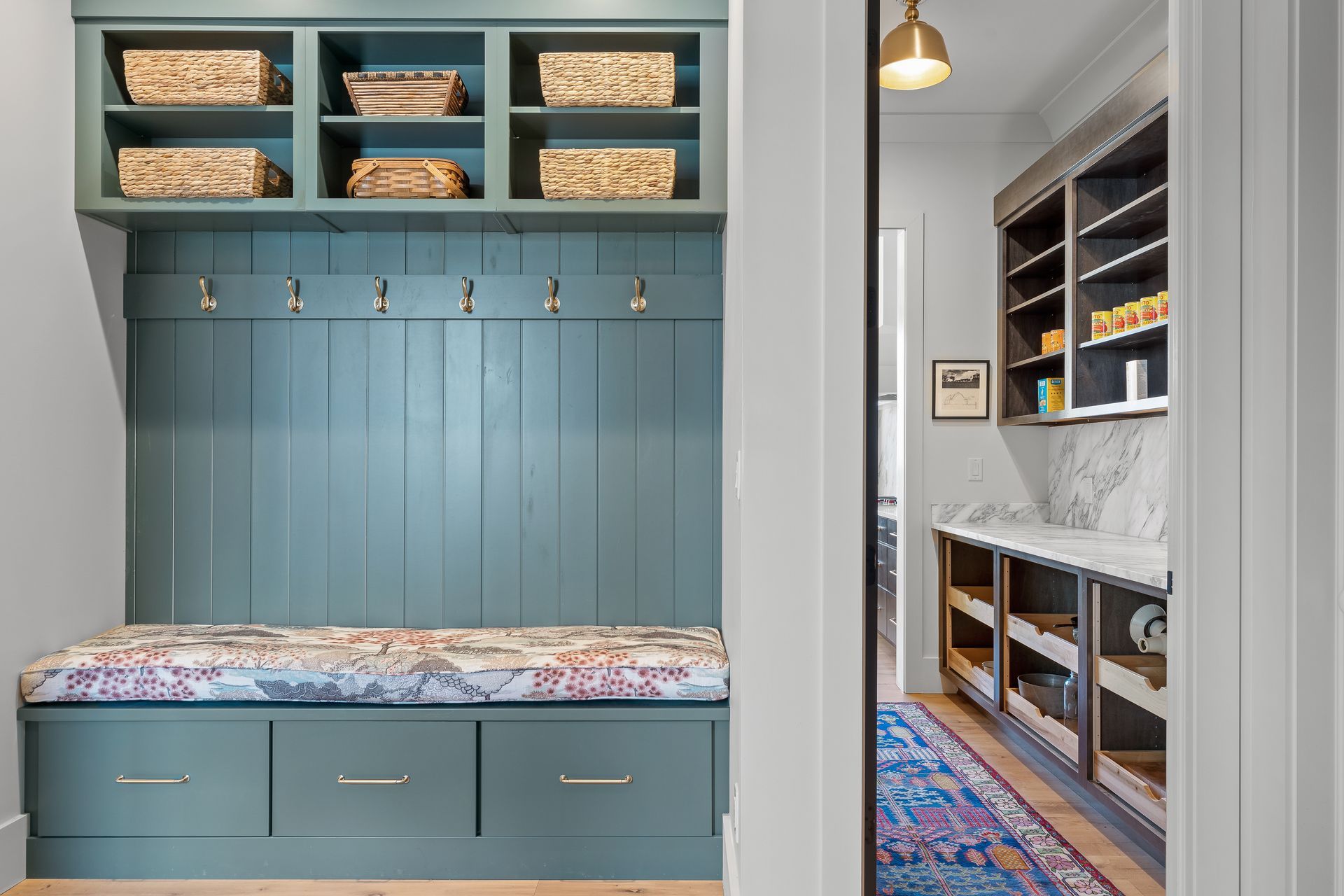 Blue built-in entryway with storage, hooks, and bench. Pantry with shelves visible in doorway.