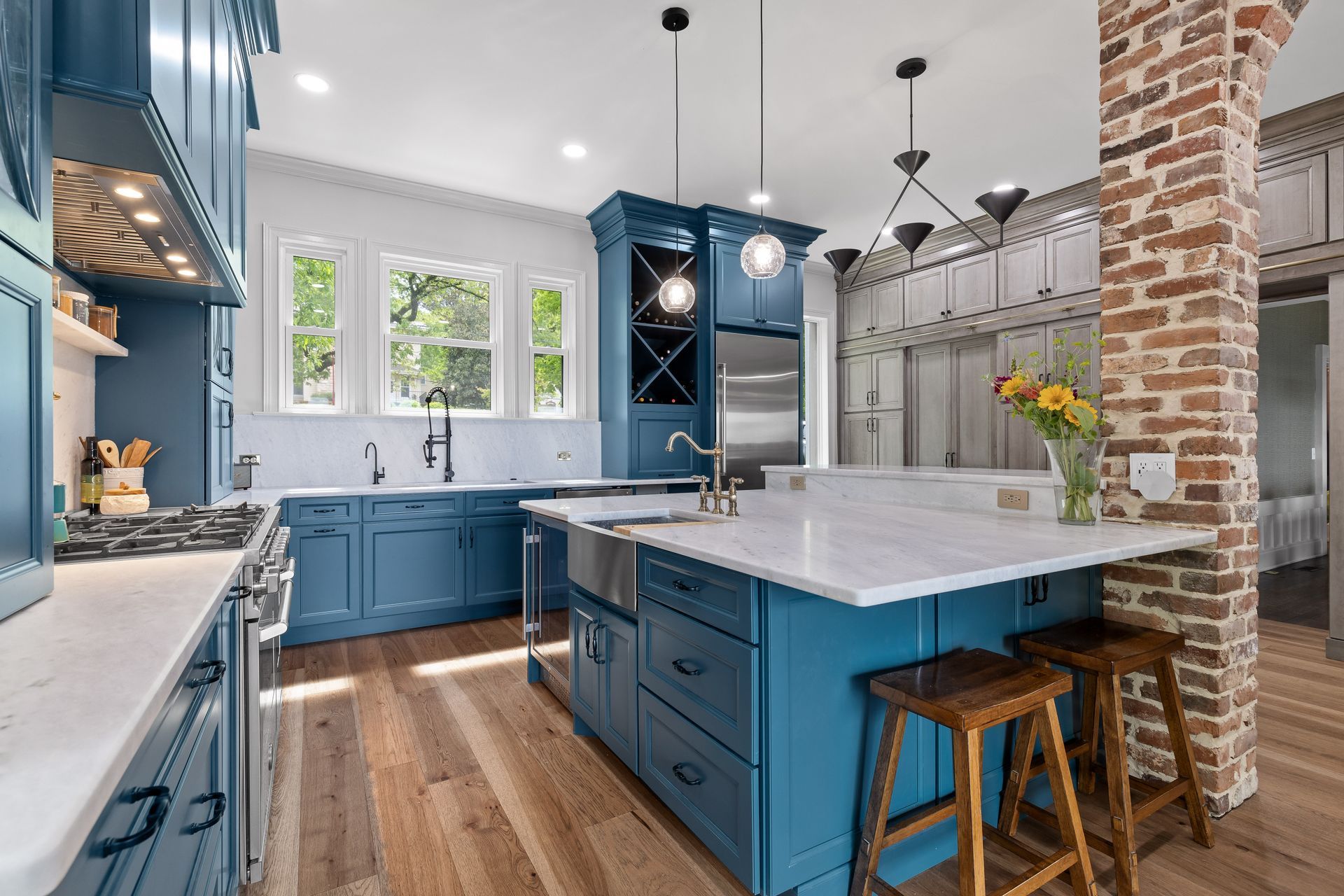 Blue kitchen with island, white countertops, wooden floors, and brick column.
