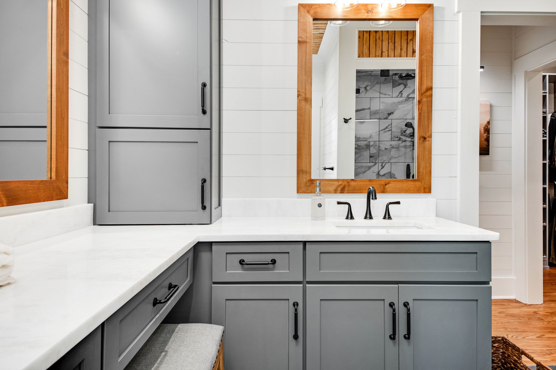 Gray bathroom with white countertop, wooden-framed mirror, black faucet, and cabinetry.