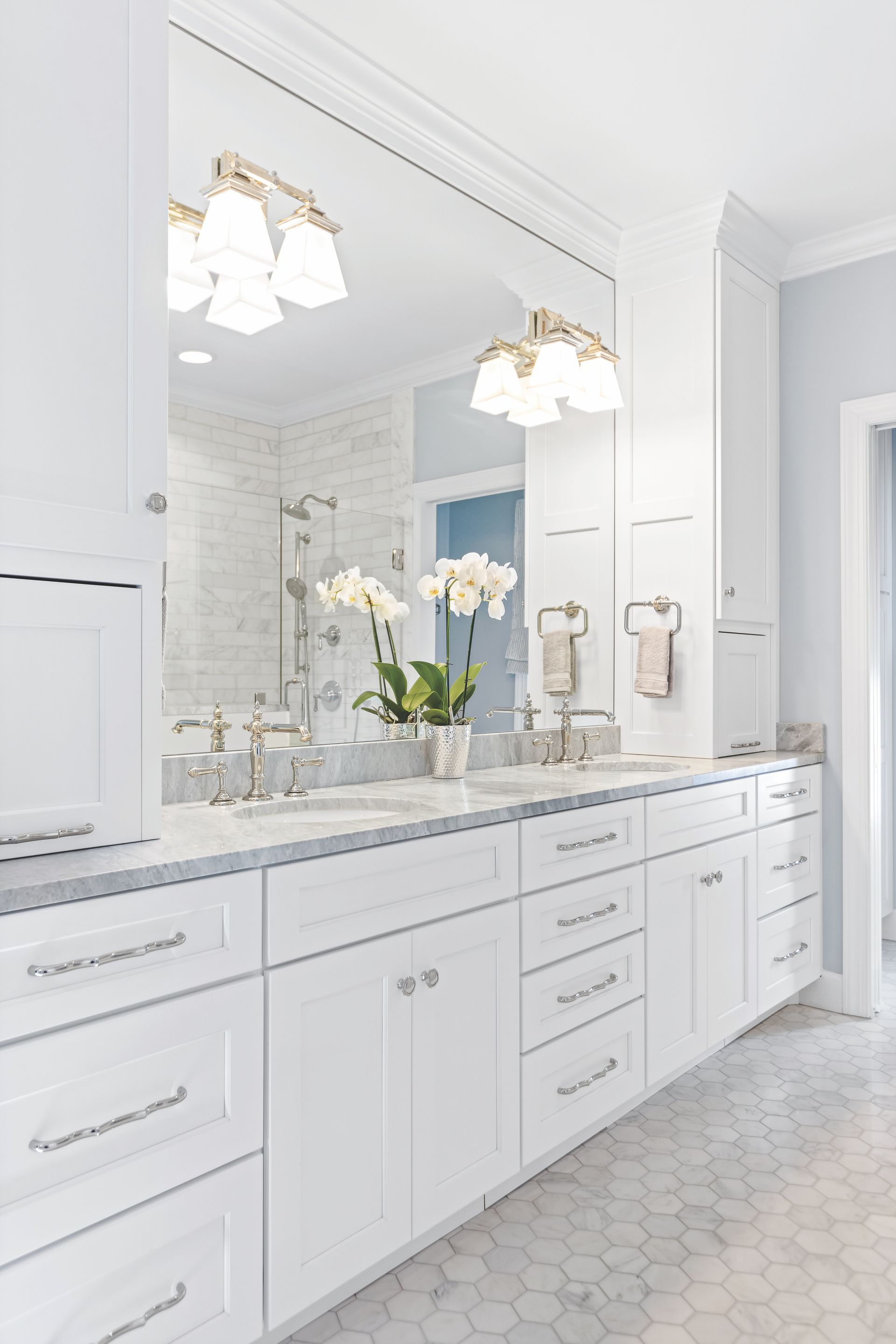 White bathroom with a large mirror over a double vanity, featuring light fixtures and marble countertops.