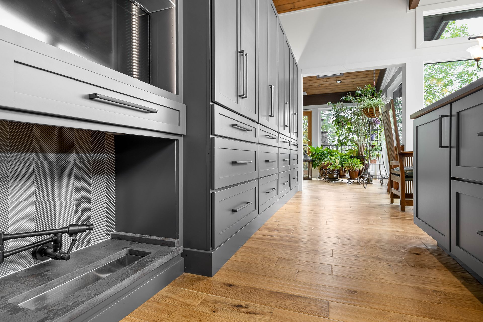 Gray cabinets with drawers and hardware line a kitchen wall, wooden floor, and fireplace.