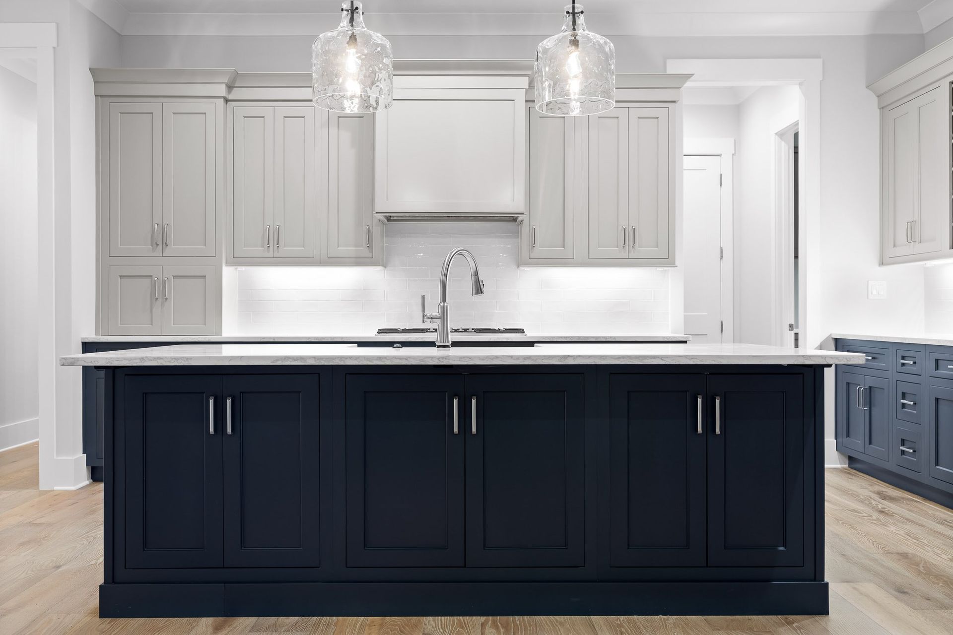 Navy island kitchen with white countertop and gray upper cabinets, two pendant lights.