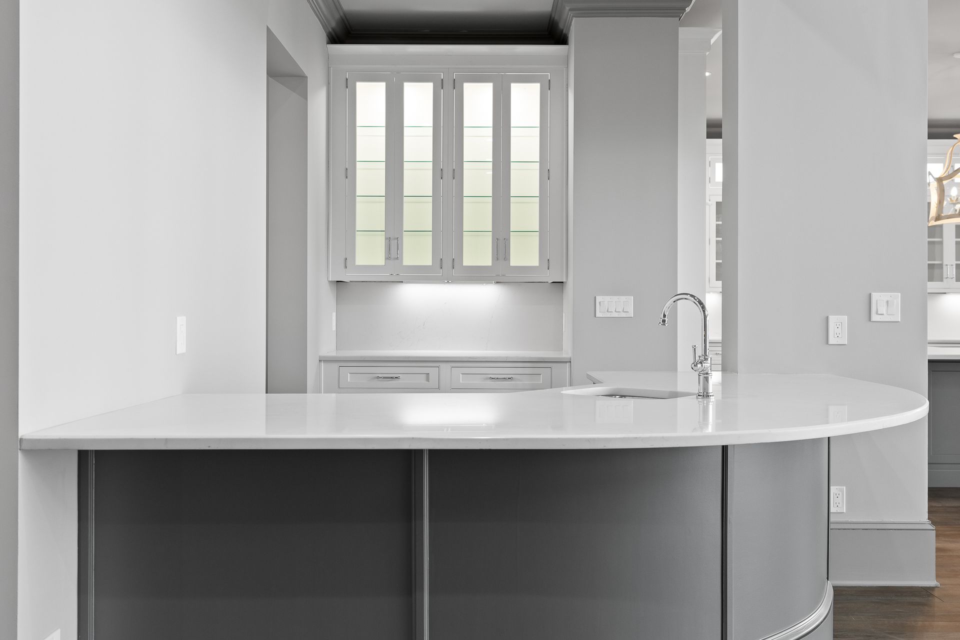 Modern gray kitchen with curved island and built-in cabinets; white countertops.