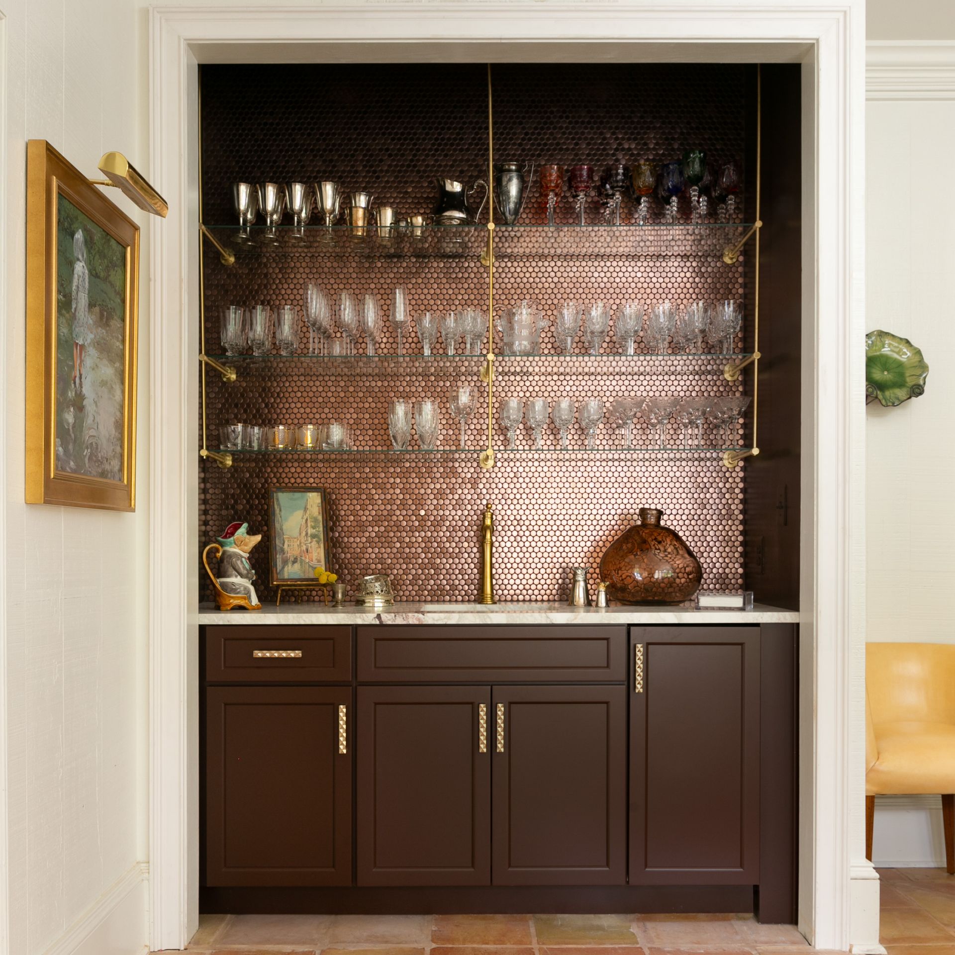 Built-in bar with copper backsplash, dark brown cabinets, brass accents, and glassware.
