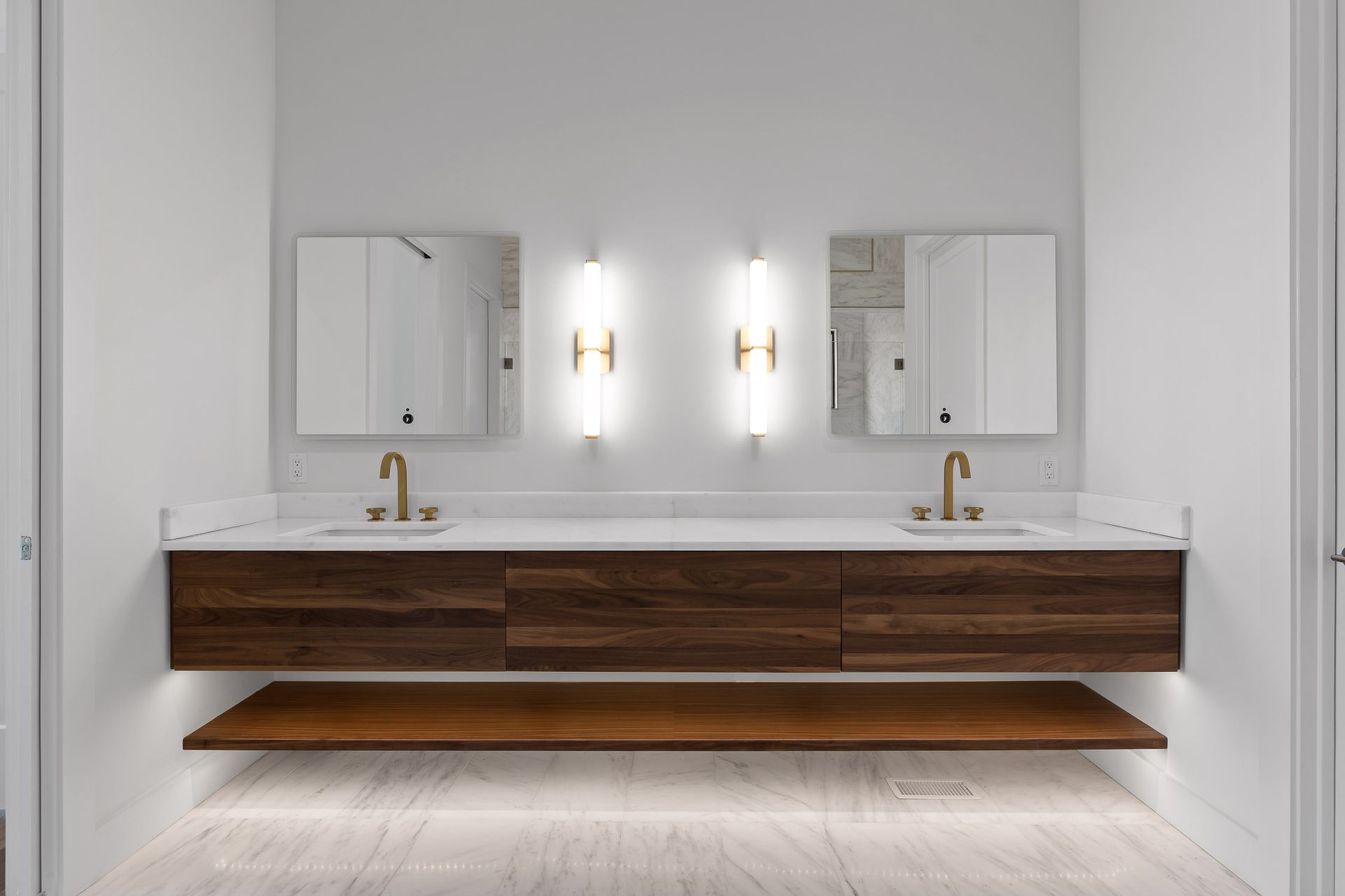Modern bathroom with floating walnut vanity, marble countertop, and brass fixtures.