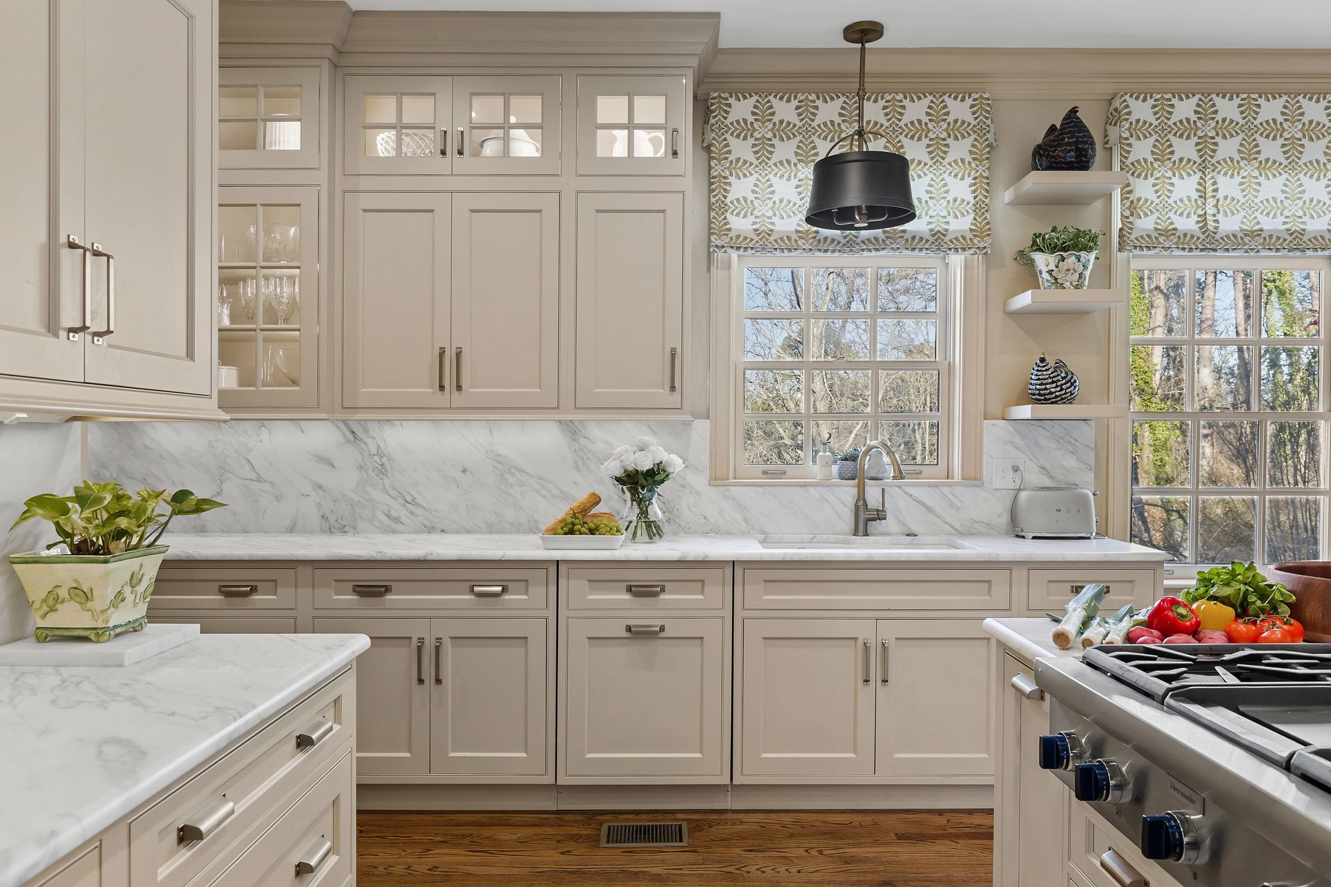 Beige kitchen with marble countertops, wooden floors, and floral window treatments.