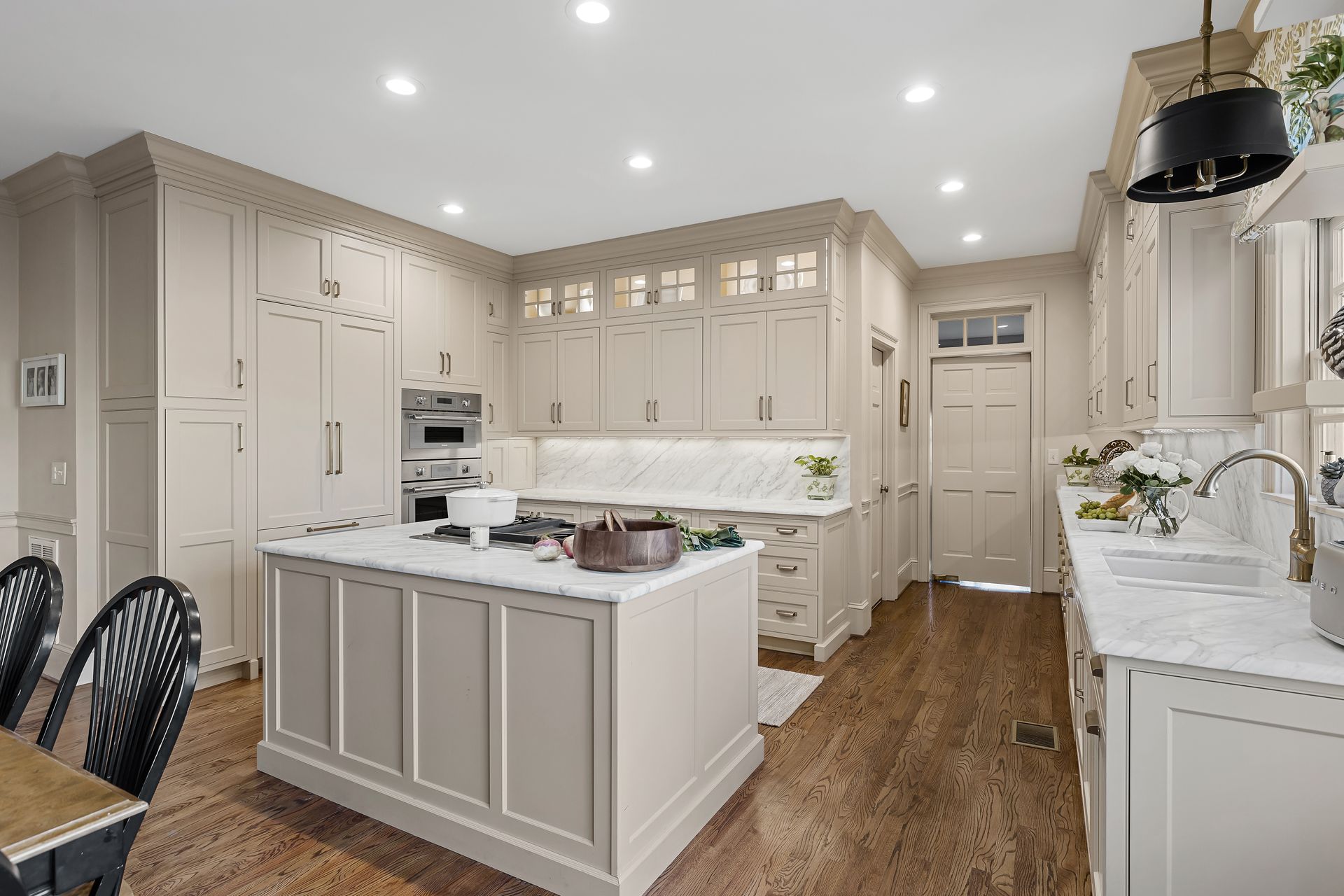 Elegant beige kitchen with island, marble countertops, stainless steel appliances, and dark wood floors.