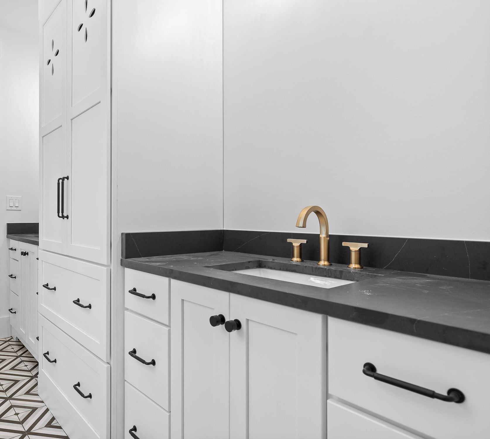 White bathroom vanity with black countertop and gold faucet.