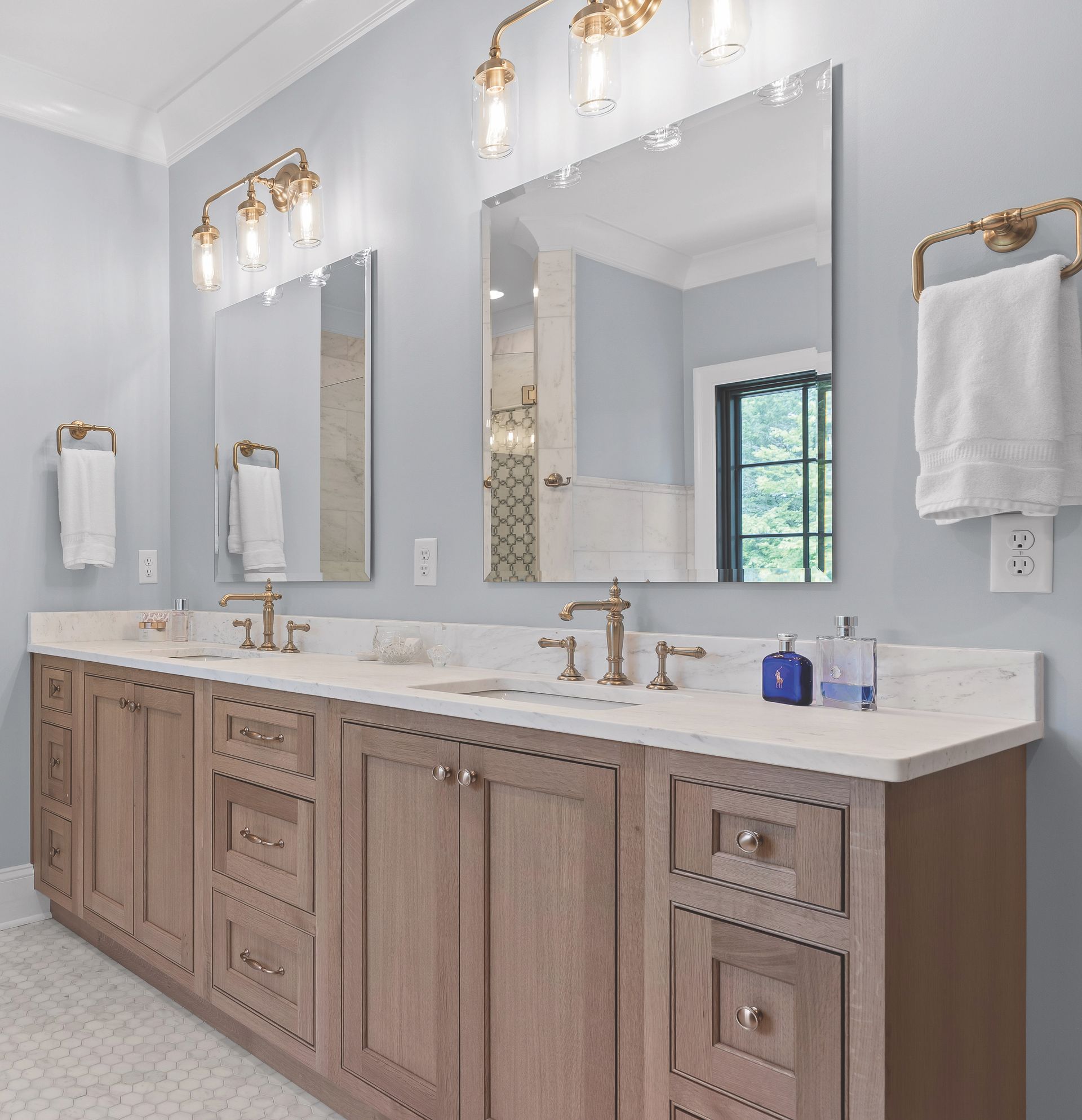Bathroom with double vanity, light blue walls, wood cabinets, gold fixtures, and mirrors.