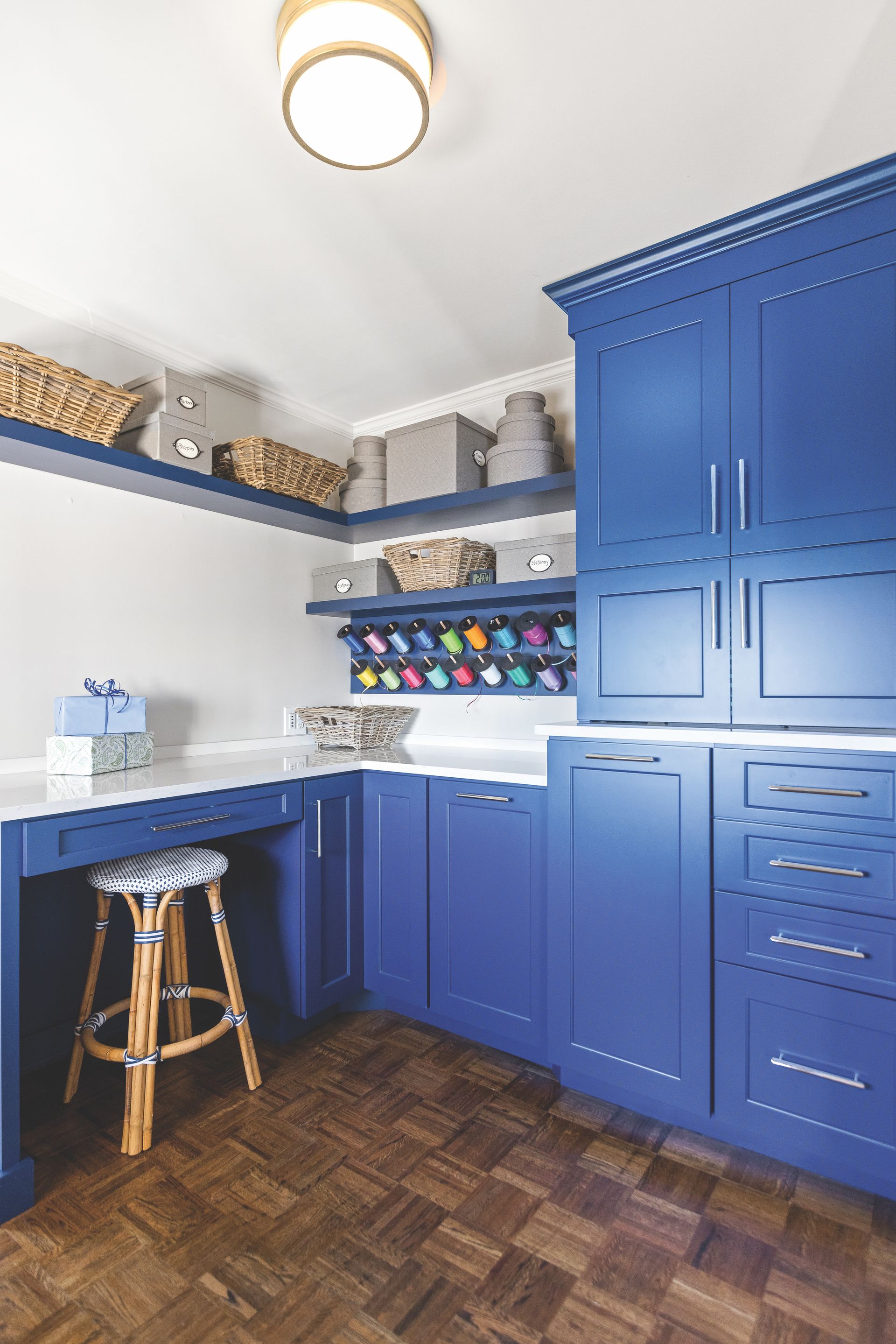 Blue craft room with cabinets, desk, and shelves, brown wood floor, and a stool.