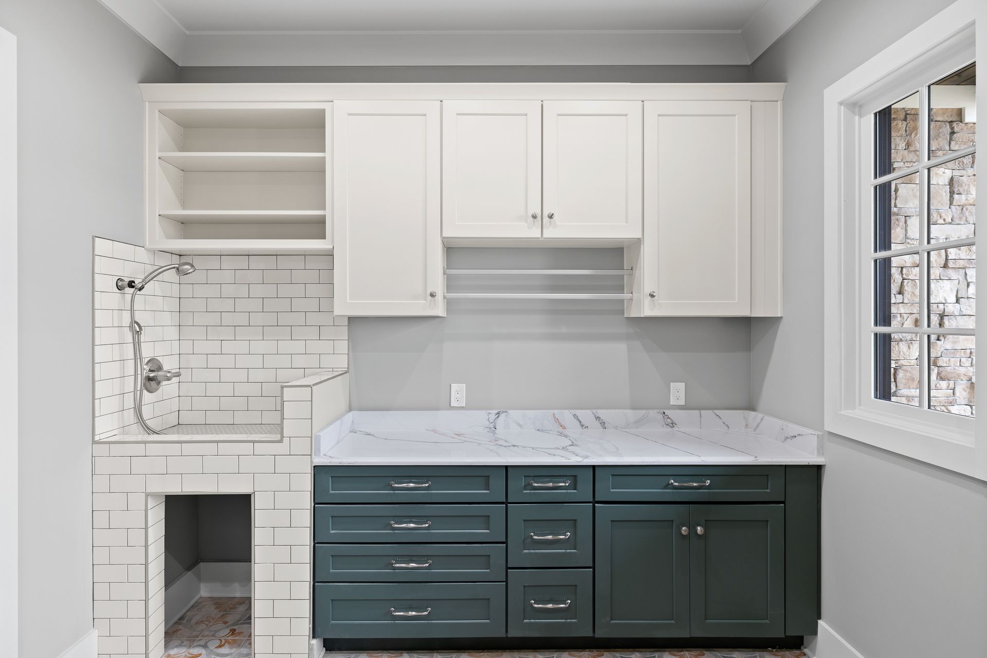 Laundry room with a dog wash station, white and teal cabinets, marble countertop, and a window.