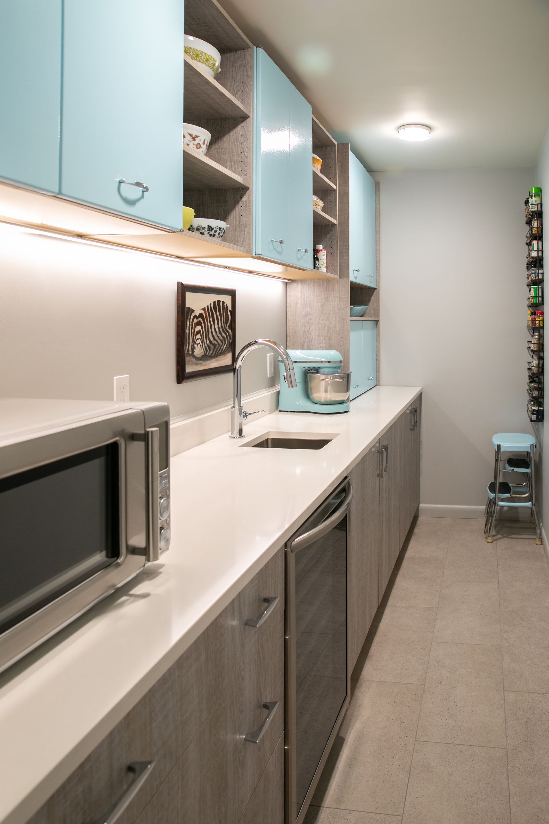 Long, narrow kitchen with light blue cabinets, light countertop, and a microwave.