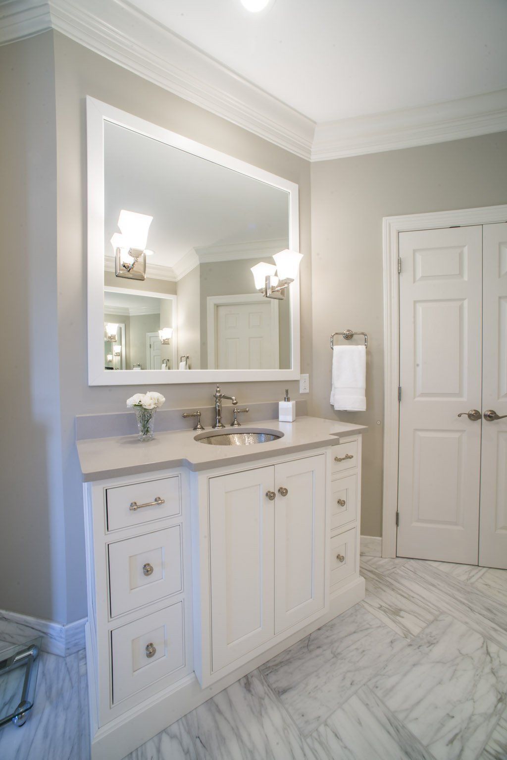 White bathroom vanity with mirror, light fixtures, and doors on marble floor.