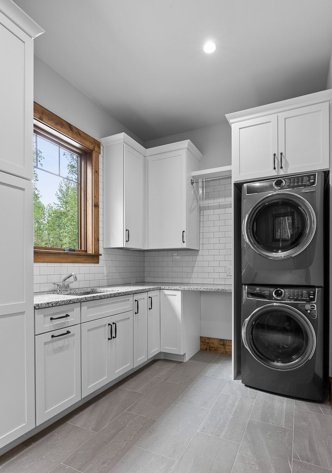 Laundry room with white cabinets, stacked black washer and dryer, and a window.