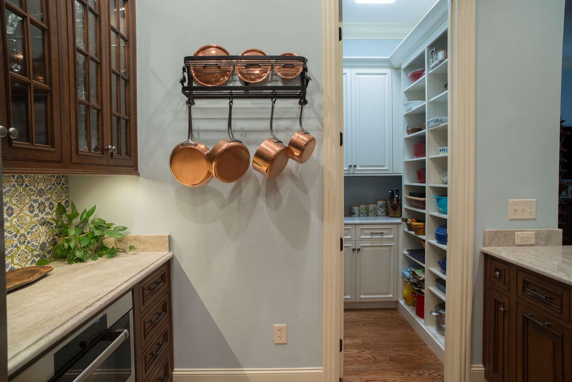 Kitchen with copper pots, pantry with shelves, brown cabinets, and light blue walls.