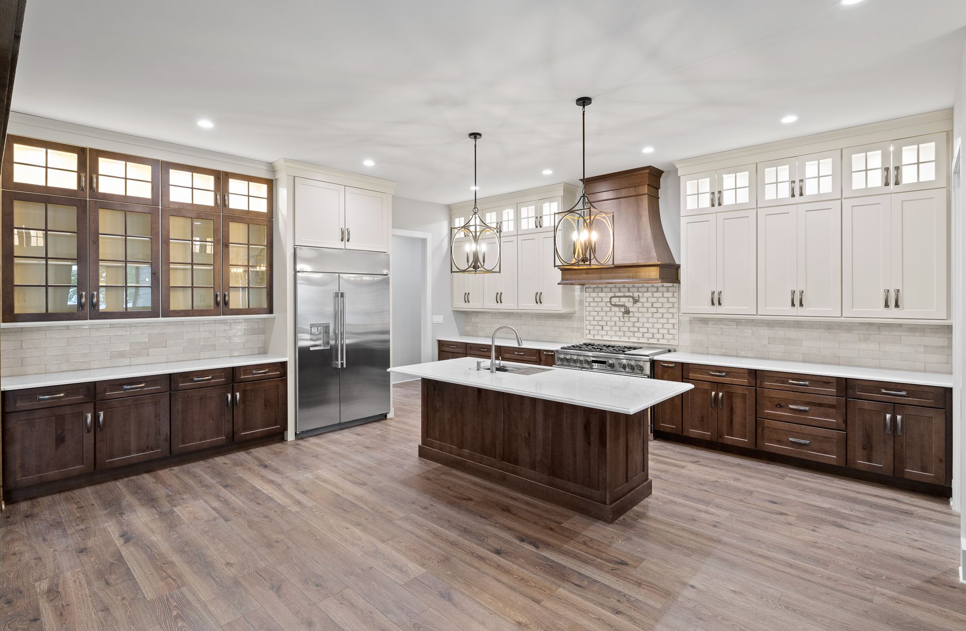 Spacious kitchen with light wood floor and dark brown cabinets, stainless steel fridge, and white island.