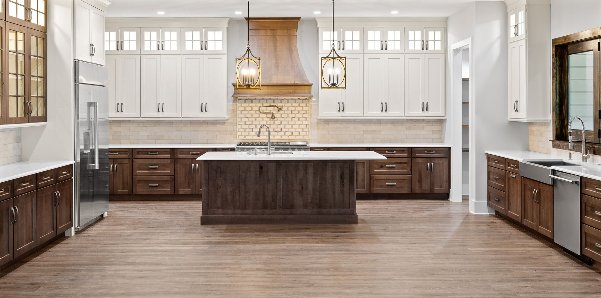 A spacious kitchen with white upper cabinets, dark lower cabinets, wooden island, and light wood floors.