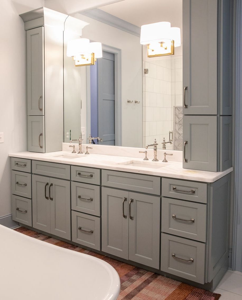 Gray bathroom vanity with tall storage cabinets, double sinks, and gold light fixtures.