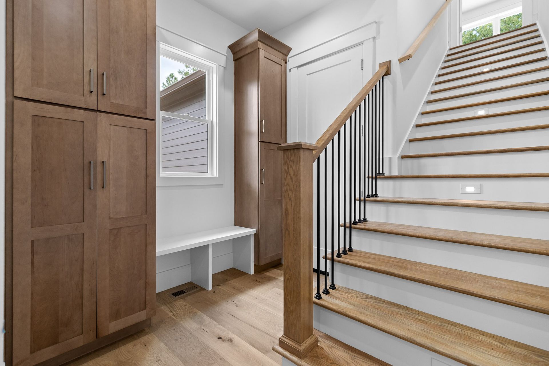 Wooden staircase and entryway with cabinets, bench, and a window.