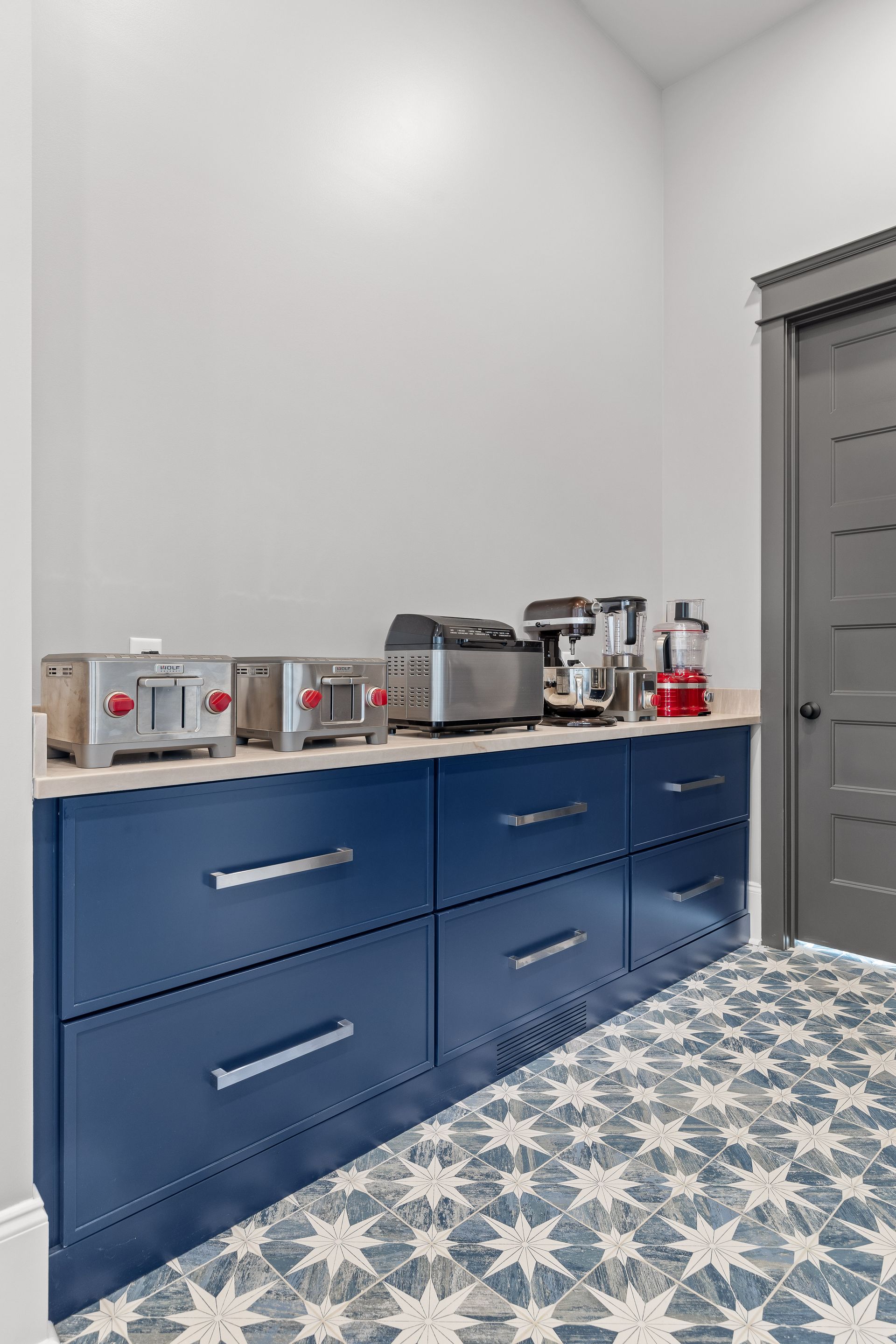 Blue cabinets with appliances on a light countertop, patterned floor, and gray door.