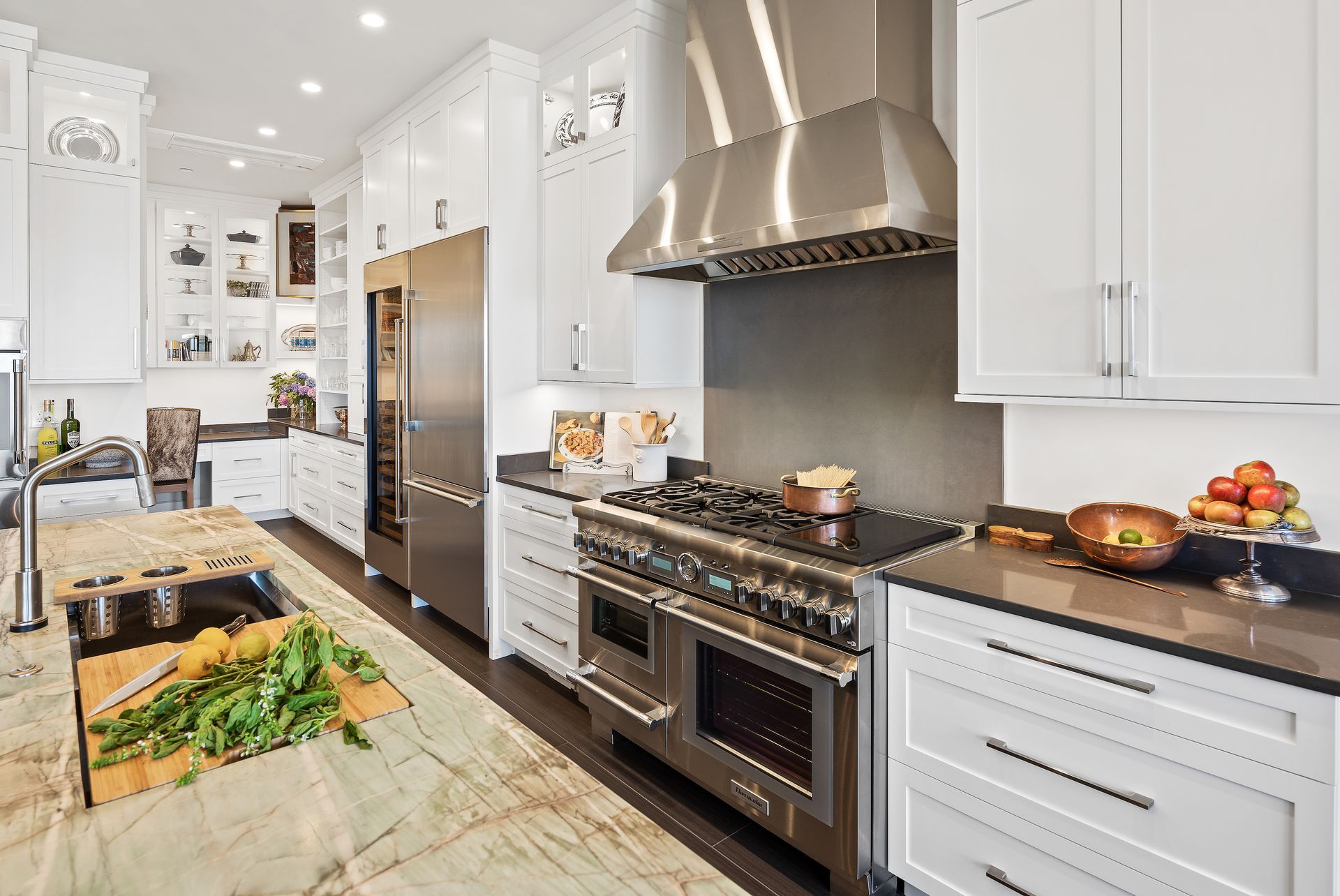 A luxurious white kitchen with stainless steel appliances, dark counters, and a marble island.