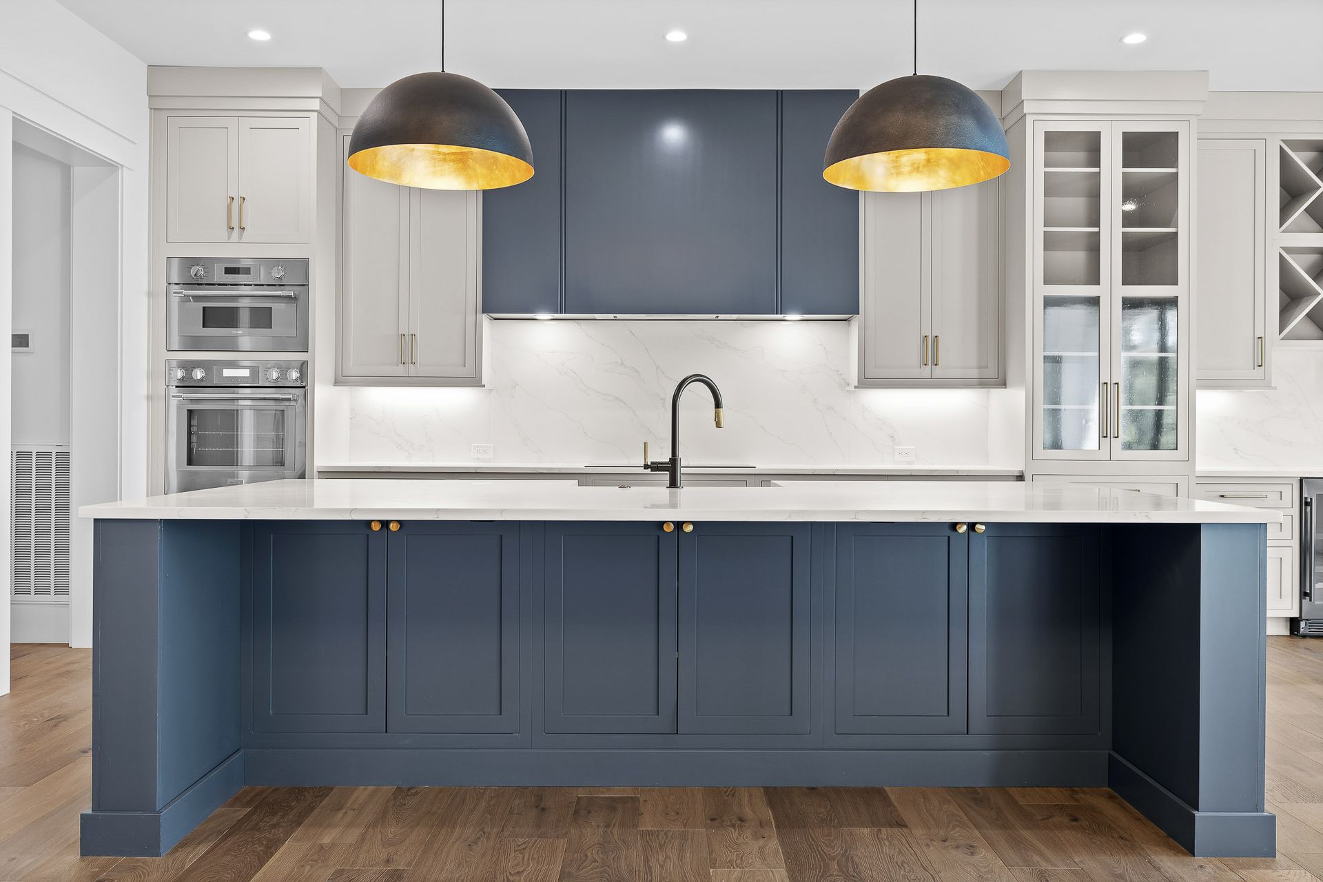 Modern kitchen with blue and white cabinetry, gold pendant lights, and a large island.