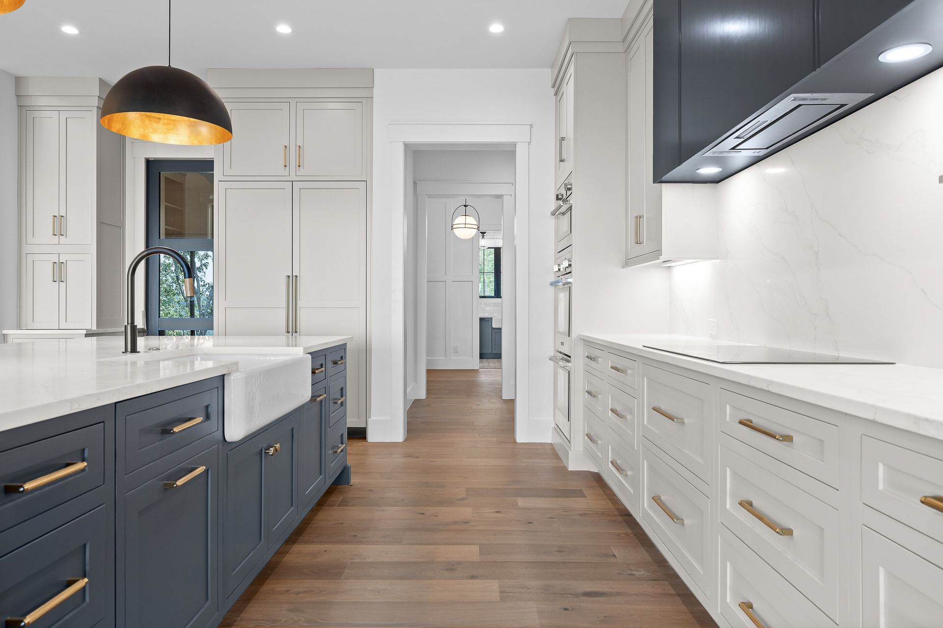 Modern kitchen with blue island, white cabinets, wood floors, and a hallway.