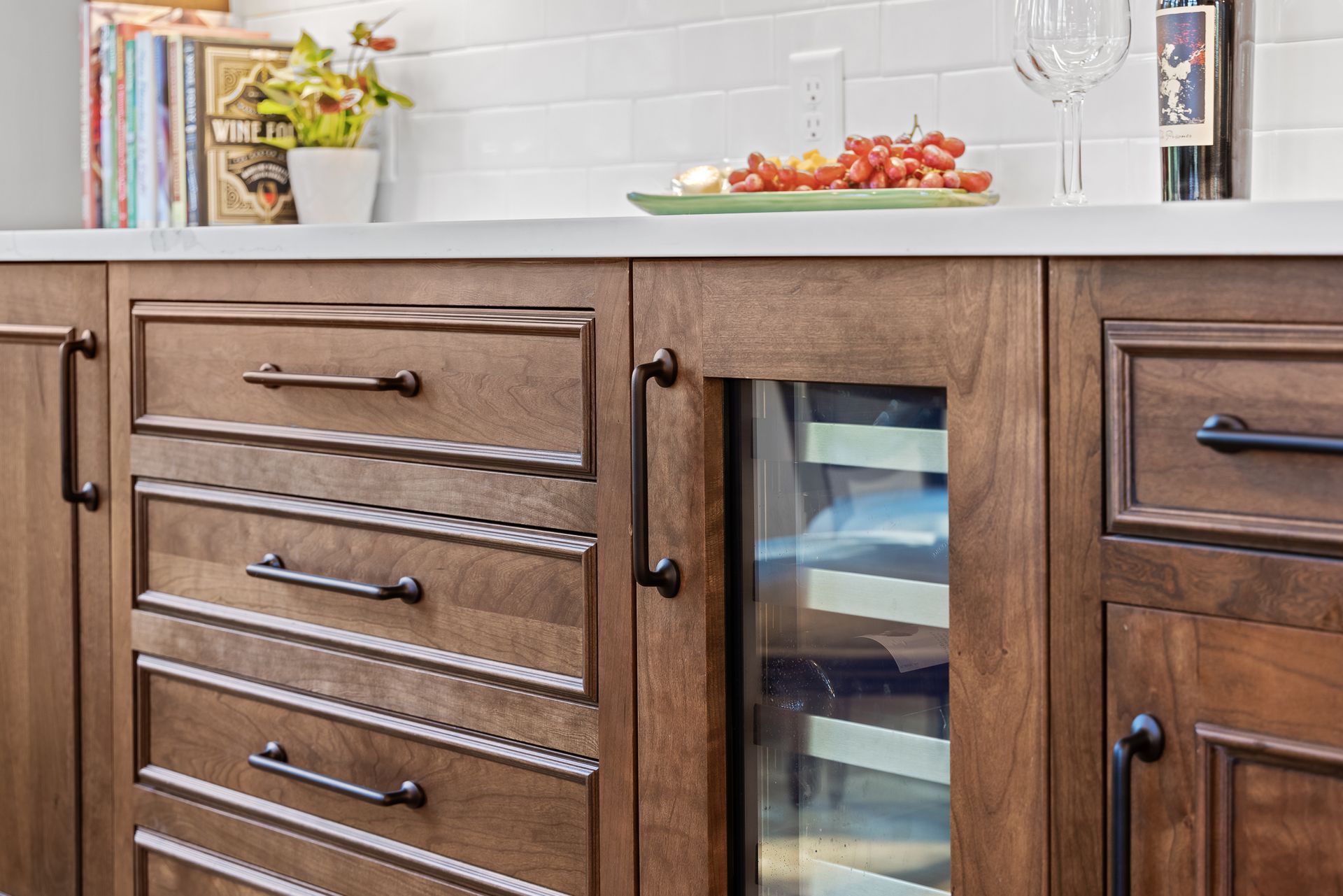 Wooden cabinets with dark handles. A built-in wine cooler is visible. Grapes and cheese sit on the counter.