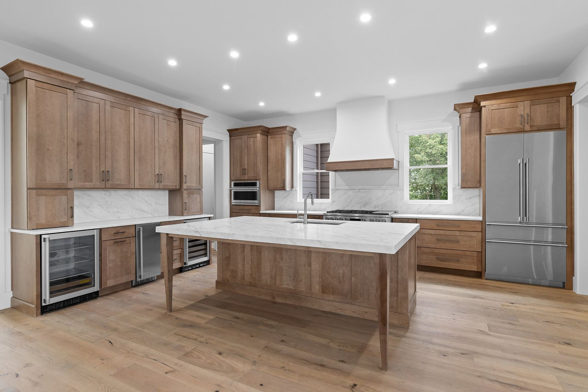 Spacious modern kitchen with light wood cabinets, marble countertops, and stainless steel appliances.