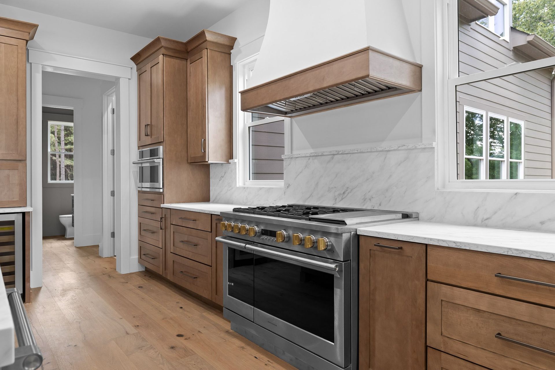 Modern kitchen with wood cabinets, stainless steel range, white countertops, and view of backyard.