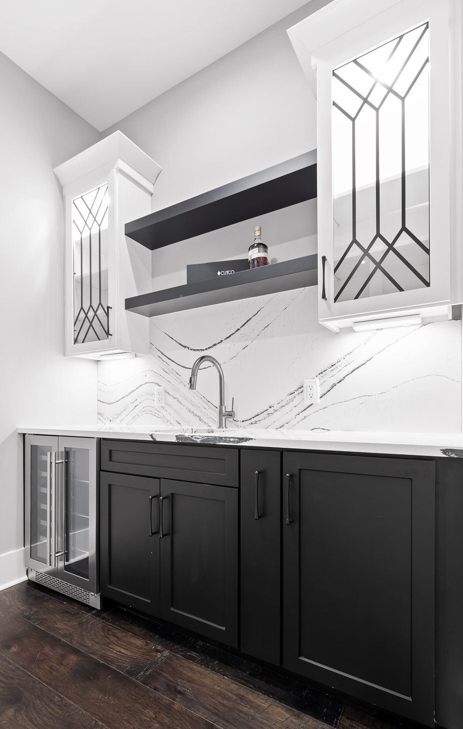 Stylish home bar with dark cabinets, white countertops, and decorative white and black backsplash.