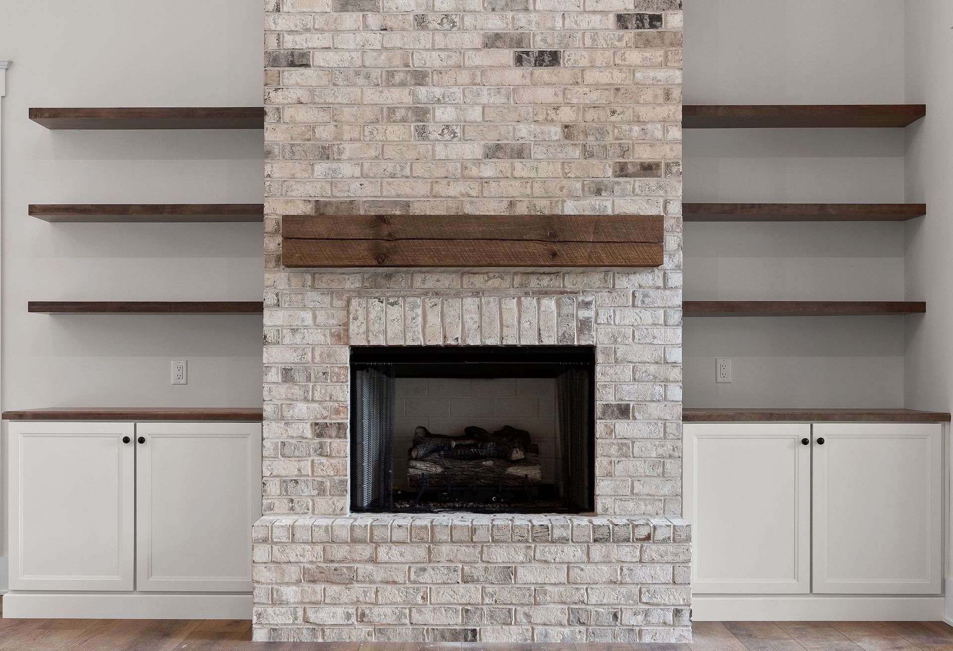 Fireplace with brick surround, wooden mantel, built-in shelves, and white cabinets.