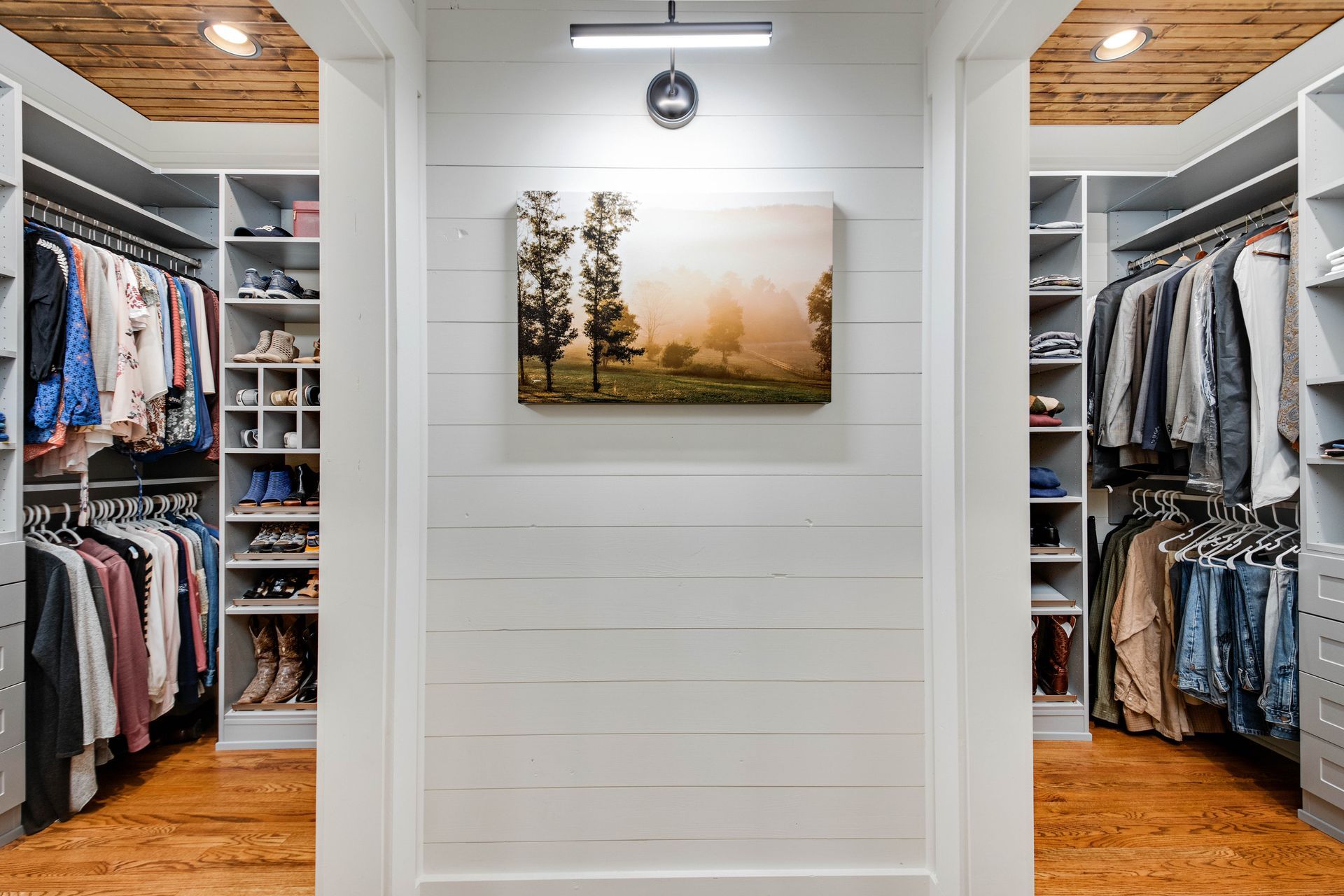 Walk-in closet with clothing racks on both sides, white walls, and art.