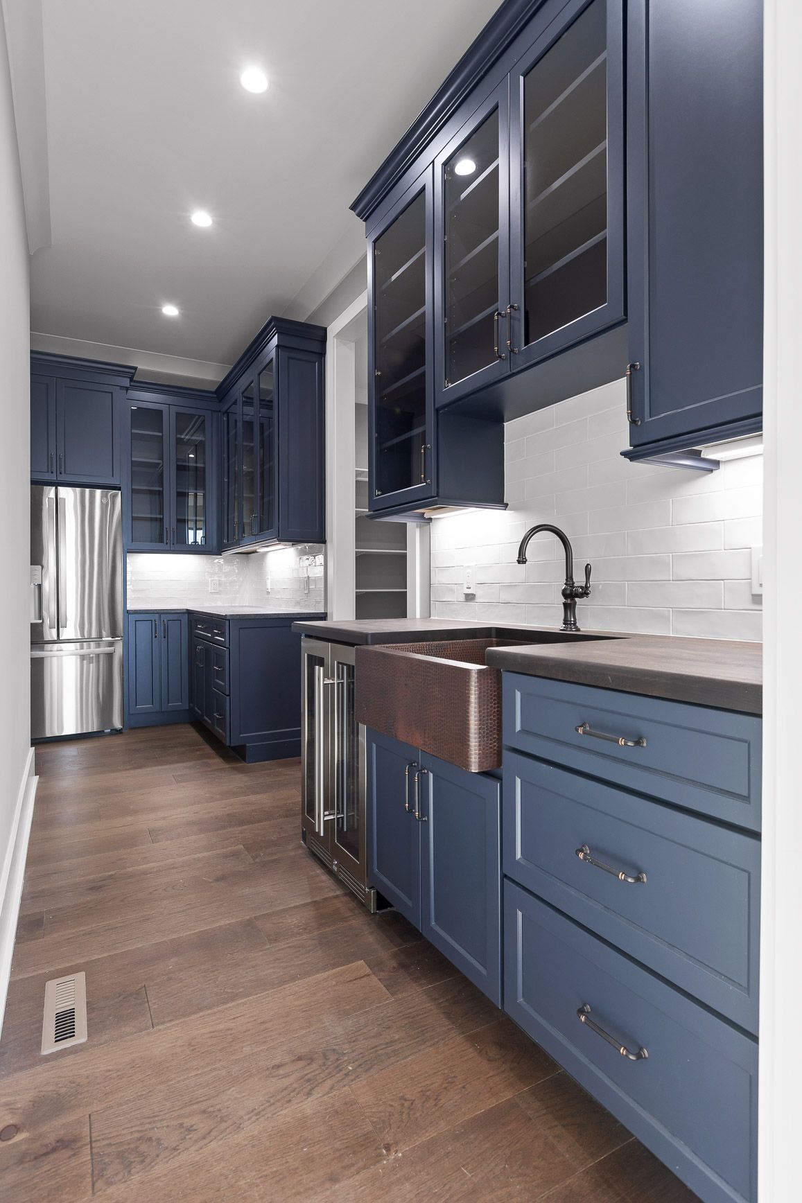 Navy blue kitchen with copper sink, glass-front cabinets, and stainless steel fridge.