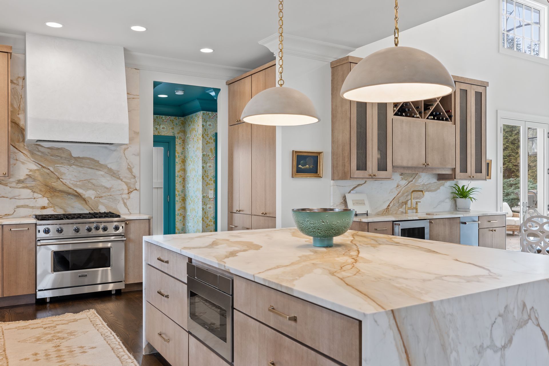 Modern kitchen with large island, light wood cabinets, and marble countertops. Two pendant lights hang above island.