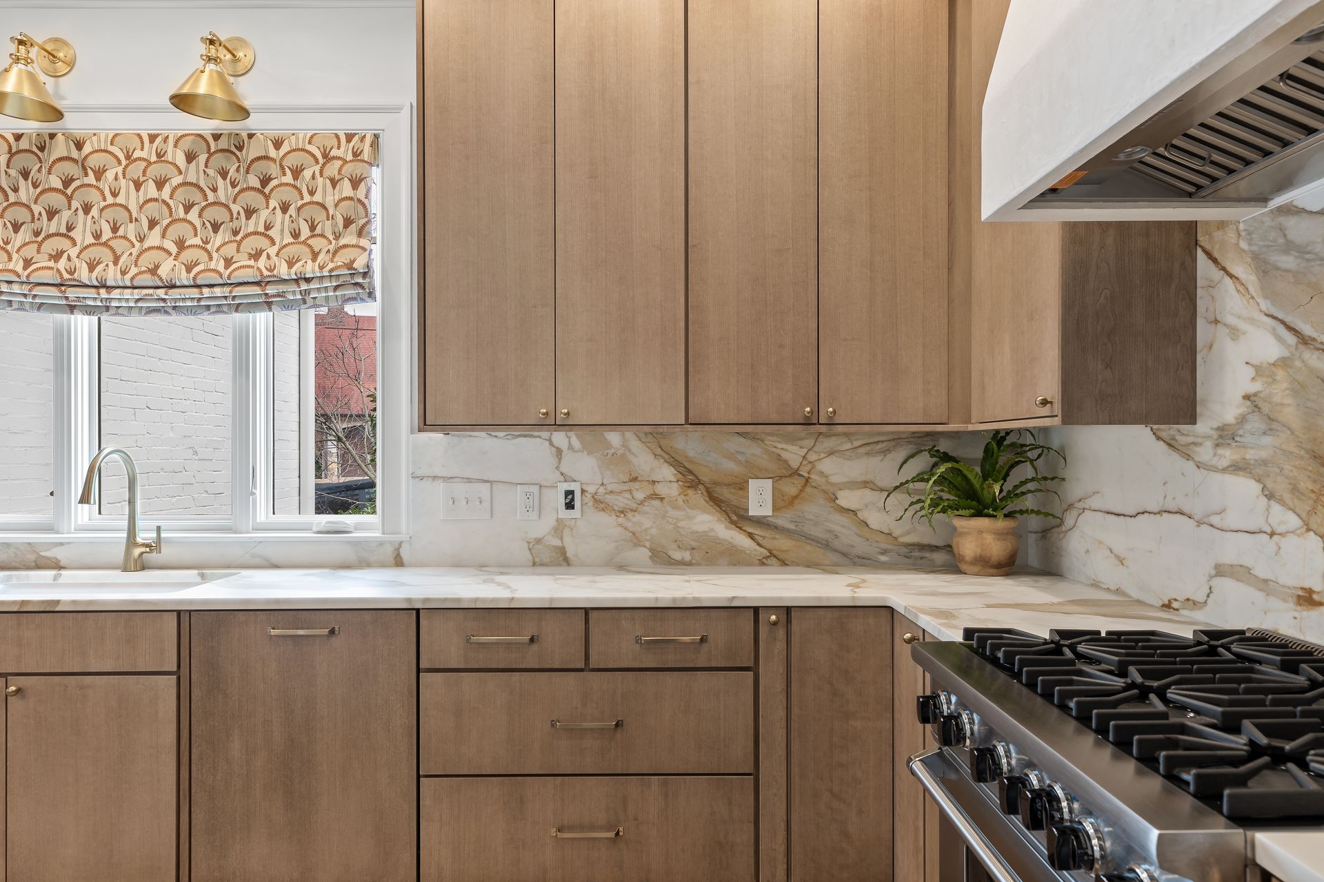 Modern kitchen with light wood cabinets, marble backsplash, and stainless steel range.