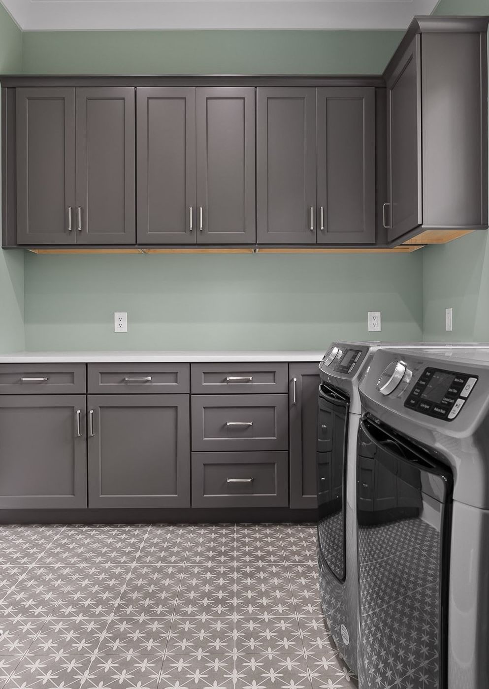 Gray laundry room with matching cabinets, light green wall, and patterned tile floor.