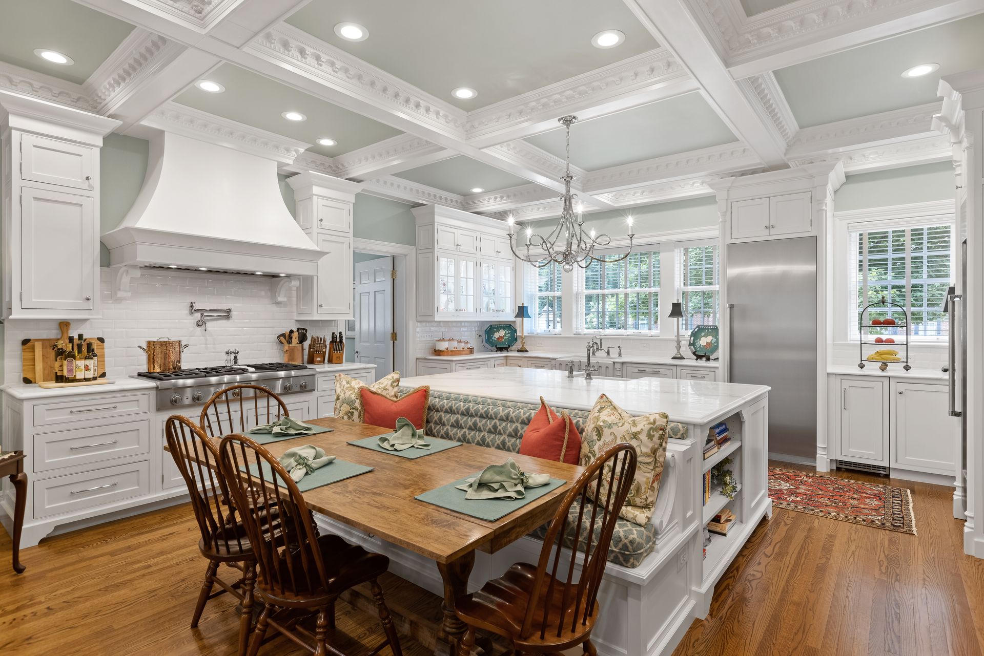Elegant white kitchen with island seating, wood table, and chandelier.