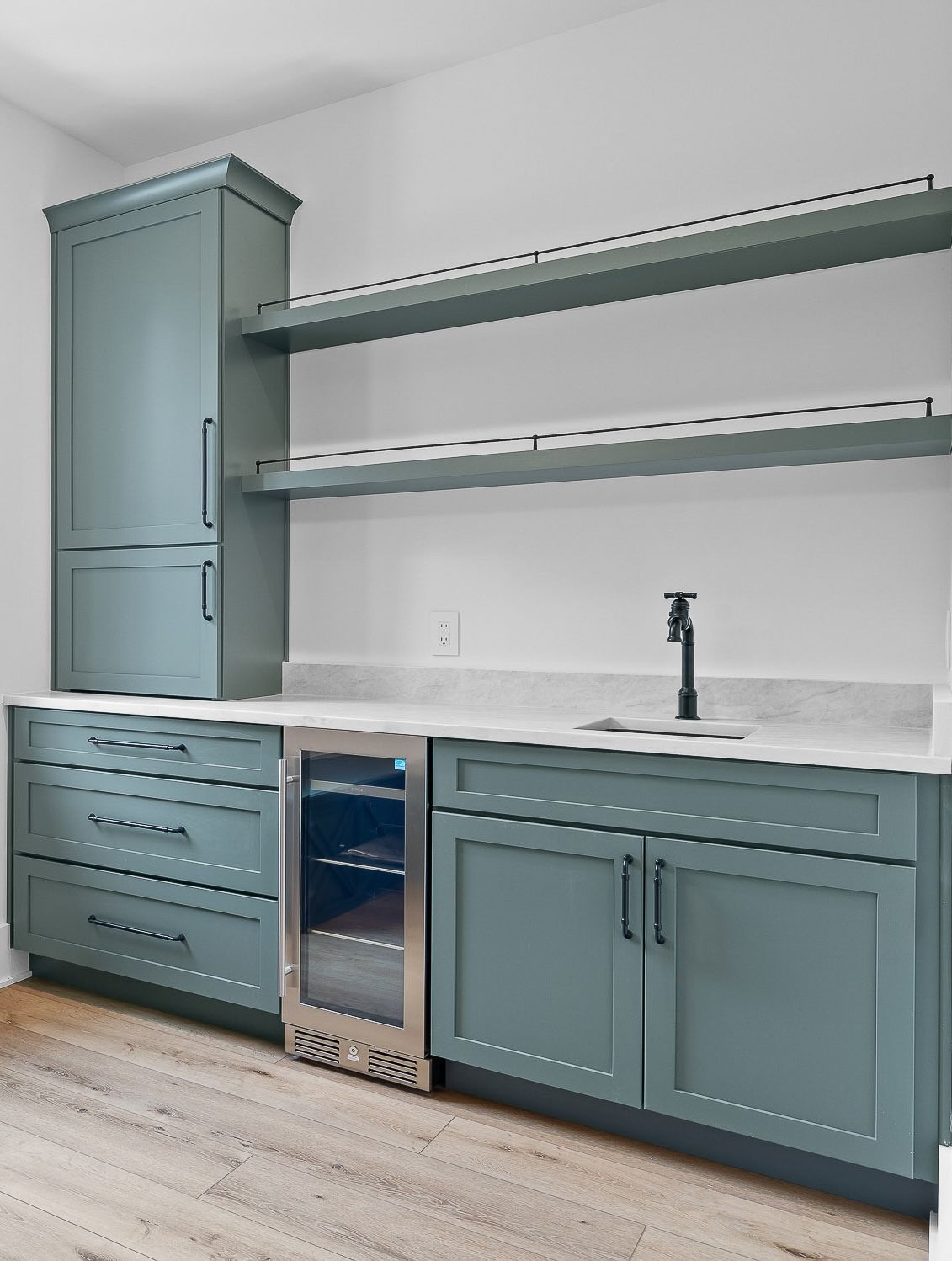 Blue-green built-in bar area with tall cabinet, shelves, and sink against white wall.