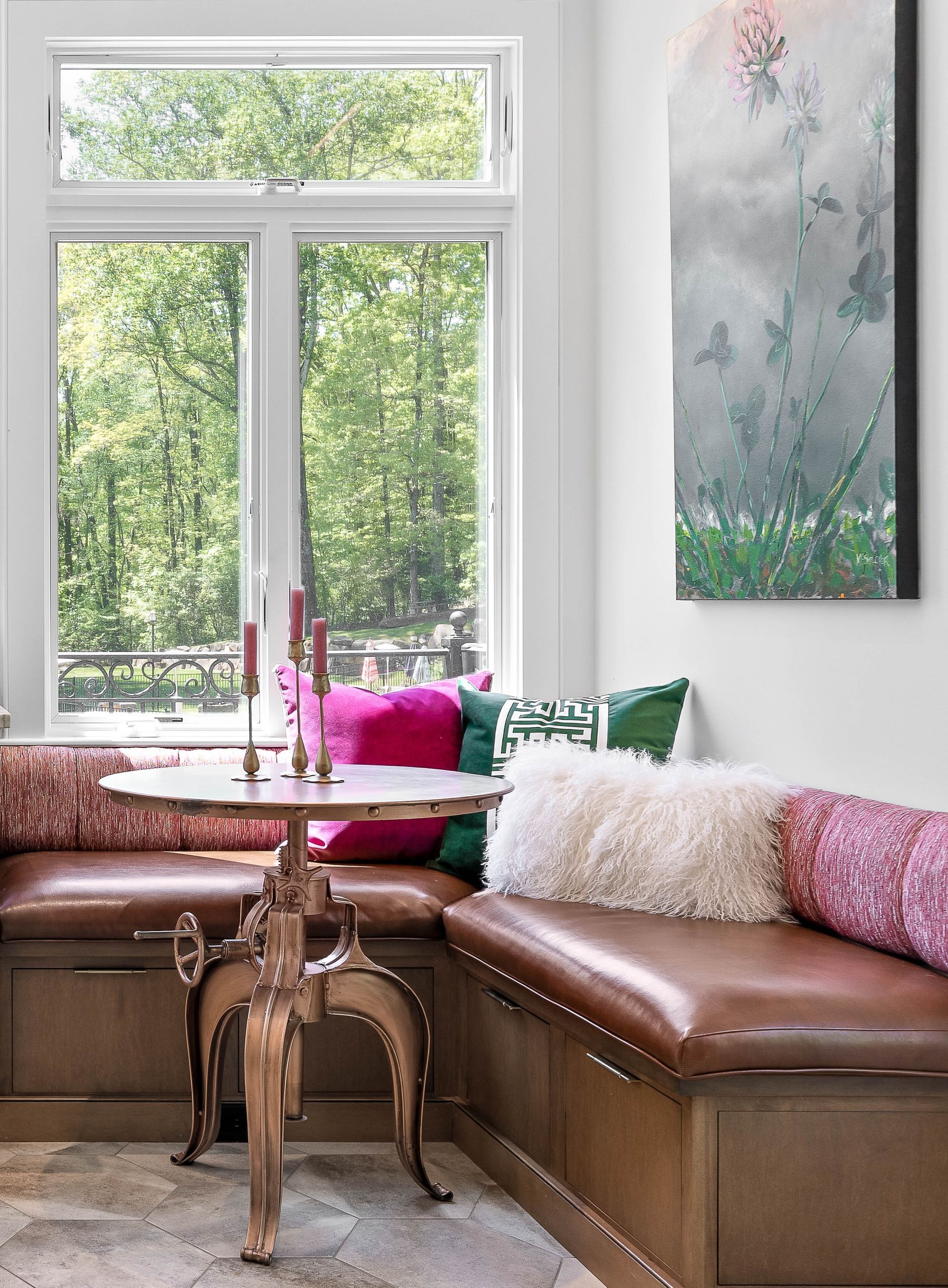 Cozy breakfast nook with leather benches, a small round table, pillows, and a window overlooking trees.