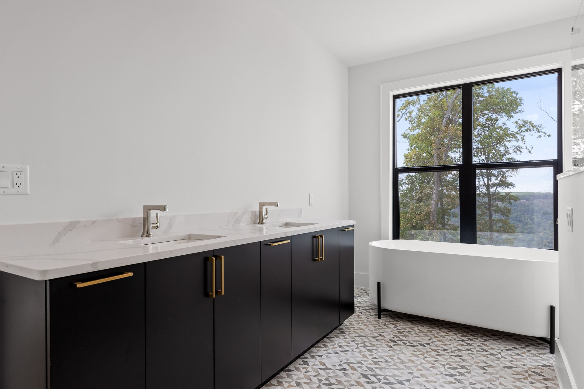 Modern bathroom with black cabinets, marble countertop, and white tub. Window reveals trees.