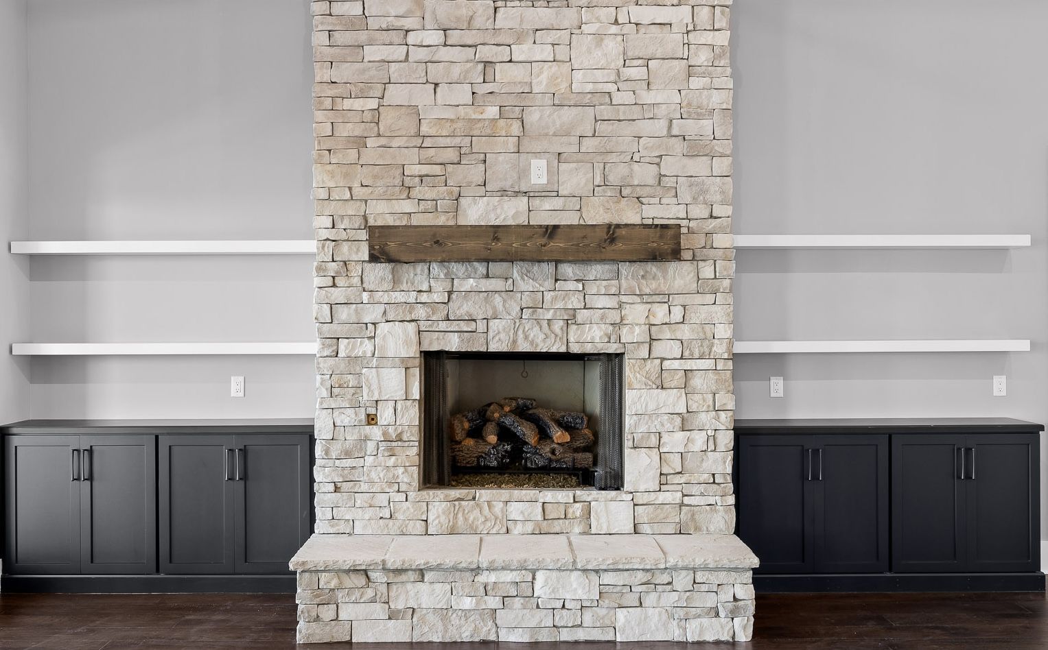 Stone fireplace with dark cabinets, white floating shelves, and gray walls.
