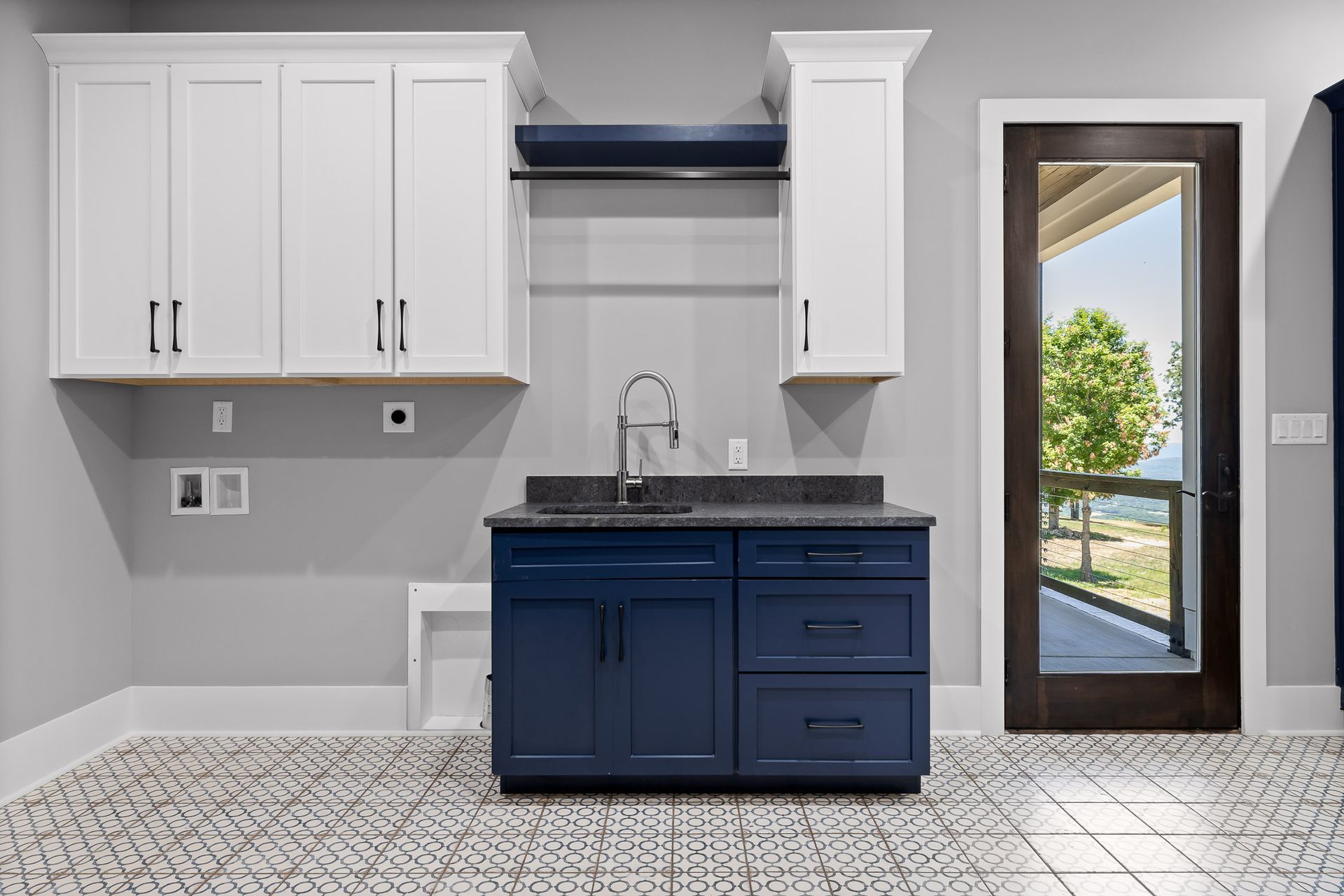 Laundry room with blue cabinets, white upper cabinets, and patterned floor. A door shows outside view.